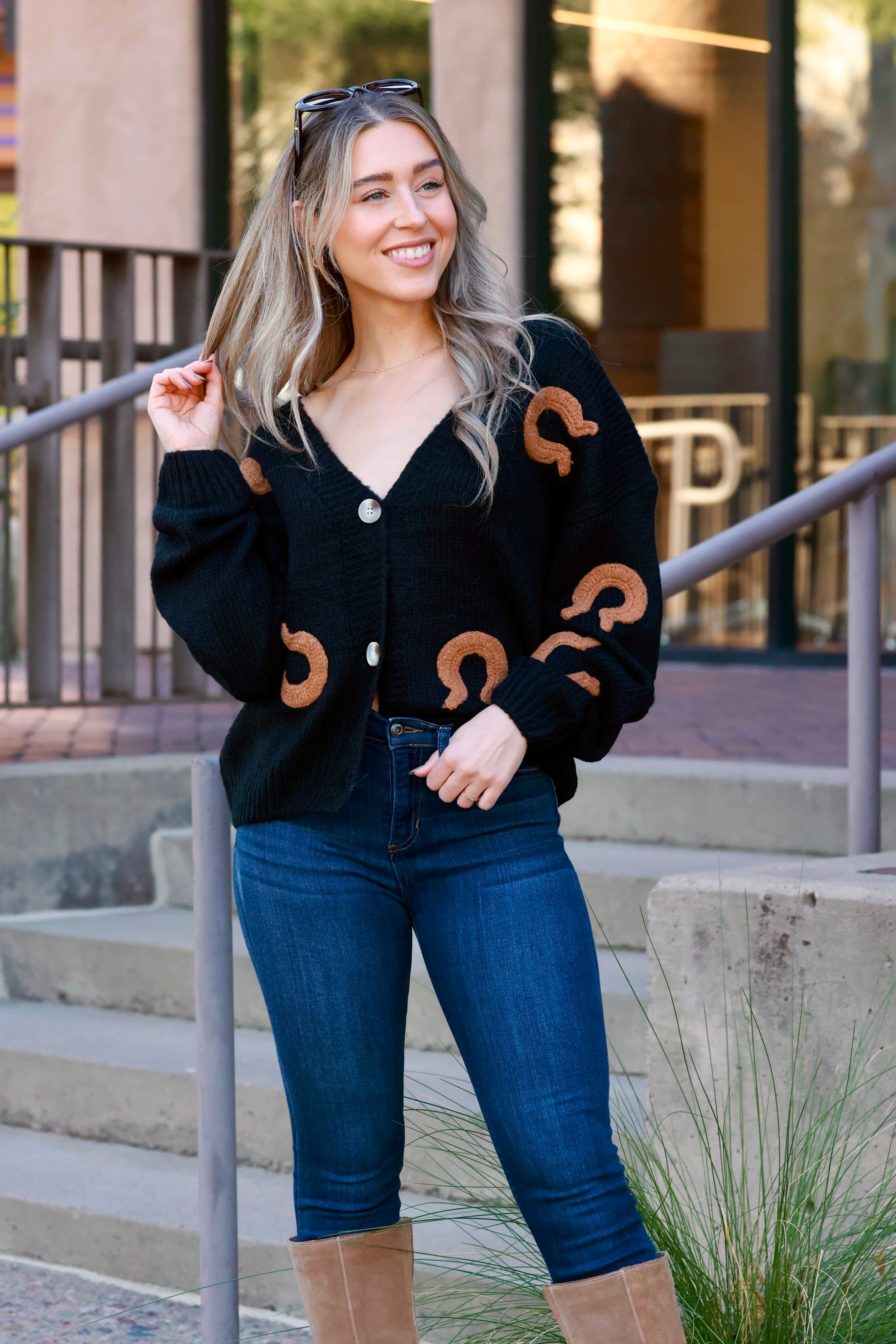 Dark-colored acrylic knit cardigan with button-front closure and deep V-neckline, featuring plush embroidered horseshoe patches throughout. Relaxed, slightly oversized fit inspired by Western style; cozy equestrian-themed fall sweater.