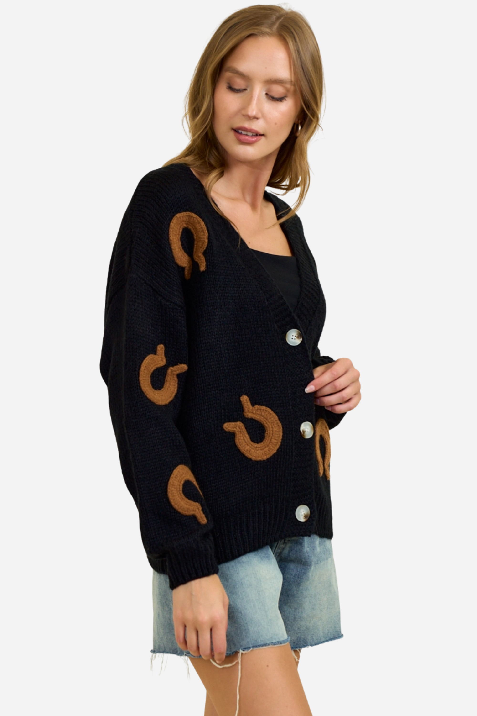 Black chunky knit cardigan with oversized brown horseshoe patches, button-front closure and deep V-neckline, styled casually with denim shorts for a relaxed equestrian-inspired look. equestrian cardigan, horseshoe print sweater, chunky knit cardigan, women’s equestrian fashion, cozy barn outfit, western inspired cardigan, horse lover gift, oversized knit sweater, casual equestrian style, layered fall equestrian look, stylish barn wear, country chic cardigan, horse themed apparel, rustic western sweater