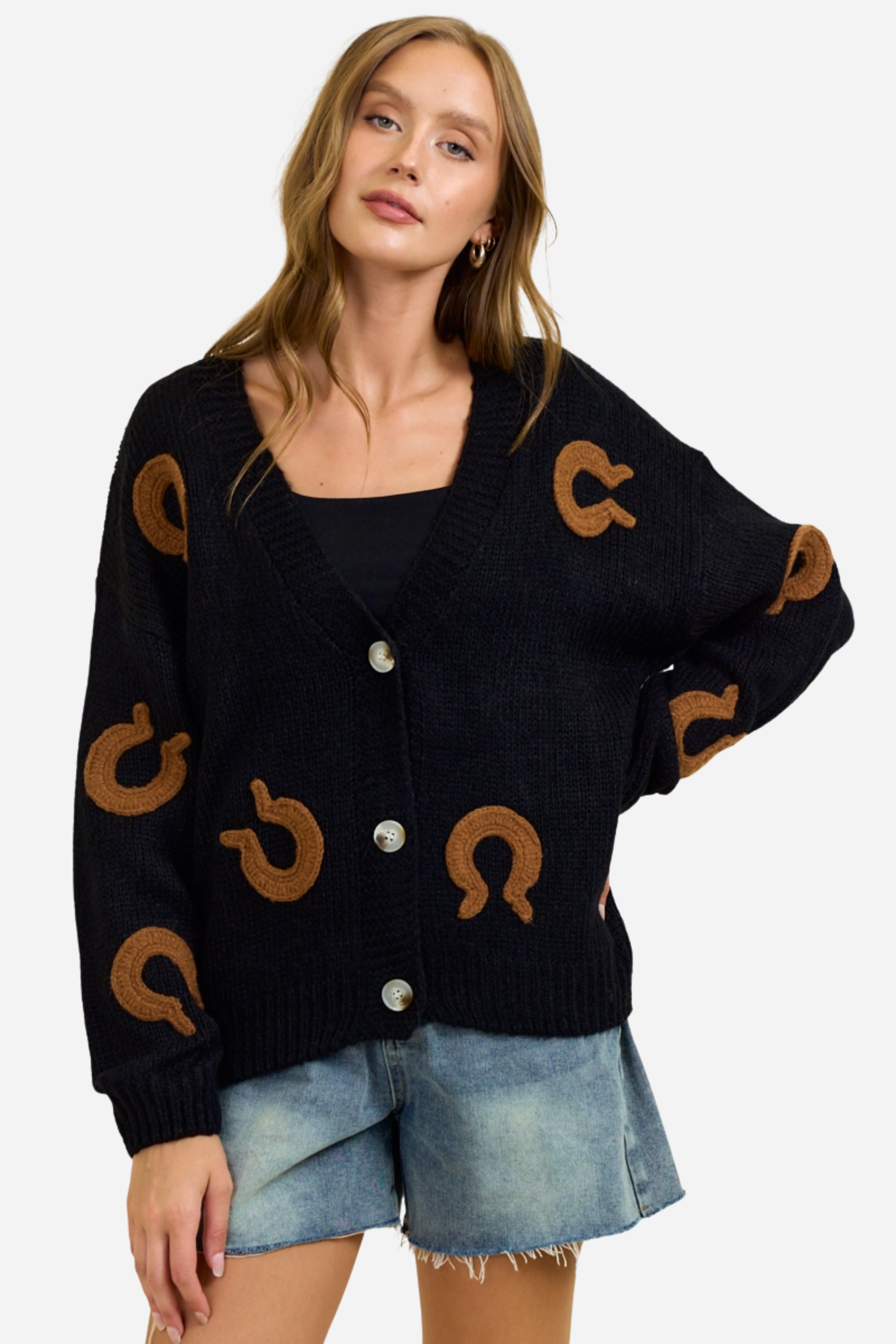 Black chunky knit cardigan with oversized brown horseshoe patches, button-front closure and deep V-neckline, styled casually with denim shorts for a relaxed equestrian-inspired look. equestrian cardigan, horseshoe print sweater, chunky knit cardigan, women’s equestrian fashion, cozy barn outfit, western inspired cardigan, horse lover gift, oversized knit sweater, casual equestrian style, layered fall equestrian look, stylish barn wear, country chic cardigan, horse themed apparel, rustic western sweater