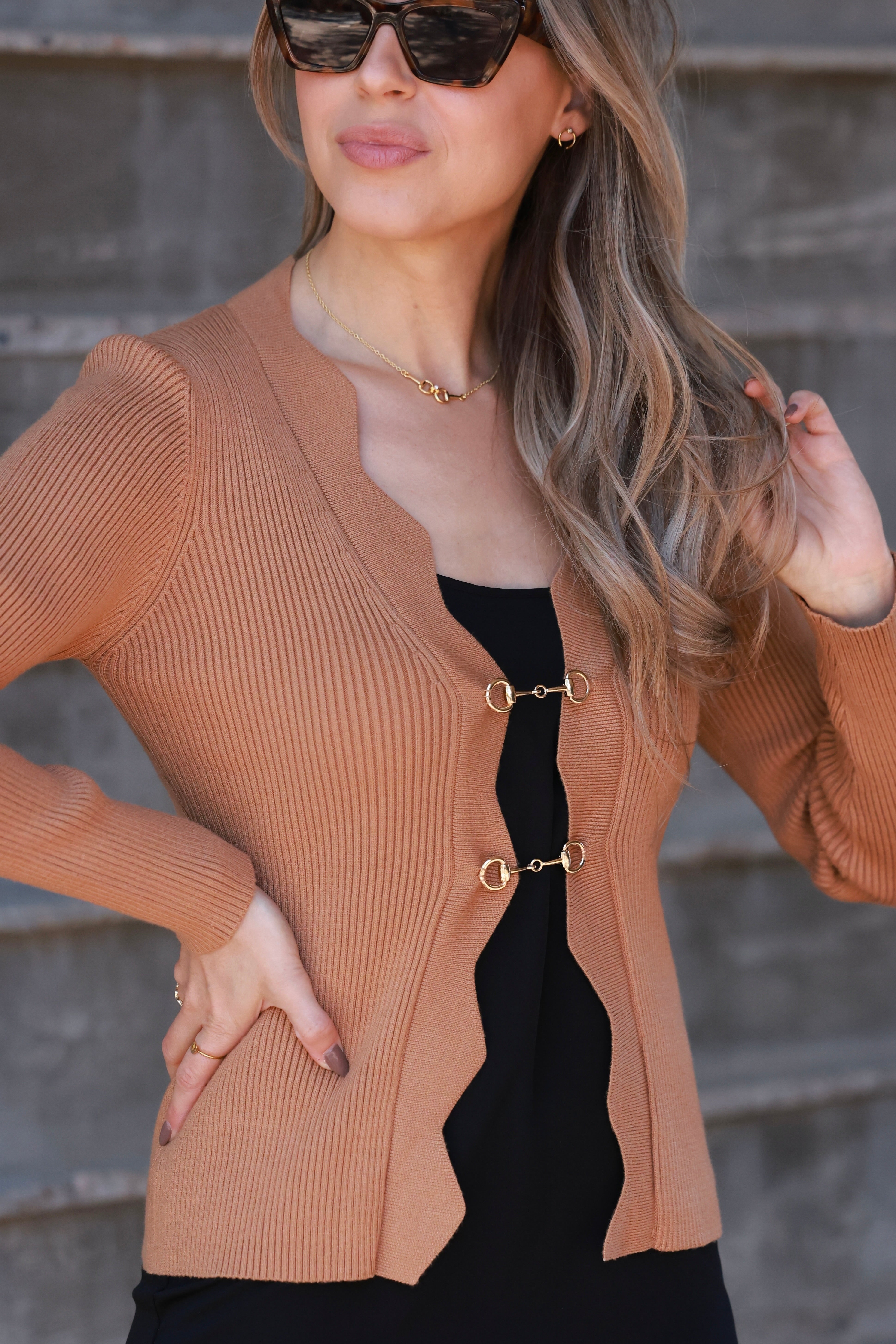 Camel-toned ribbed knit equestrian top featuring a deep scalloped neckline and two gold horsebit closures. Fitted long-sleeve cardigan-style top crafted from a poly/nylon blend, combining timeless elegance with refined equestrian detailing—perfect for fall and winter equestrian fashion.