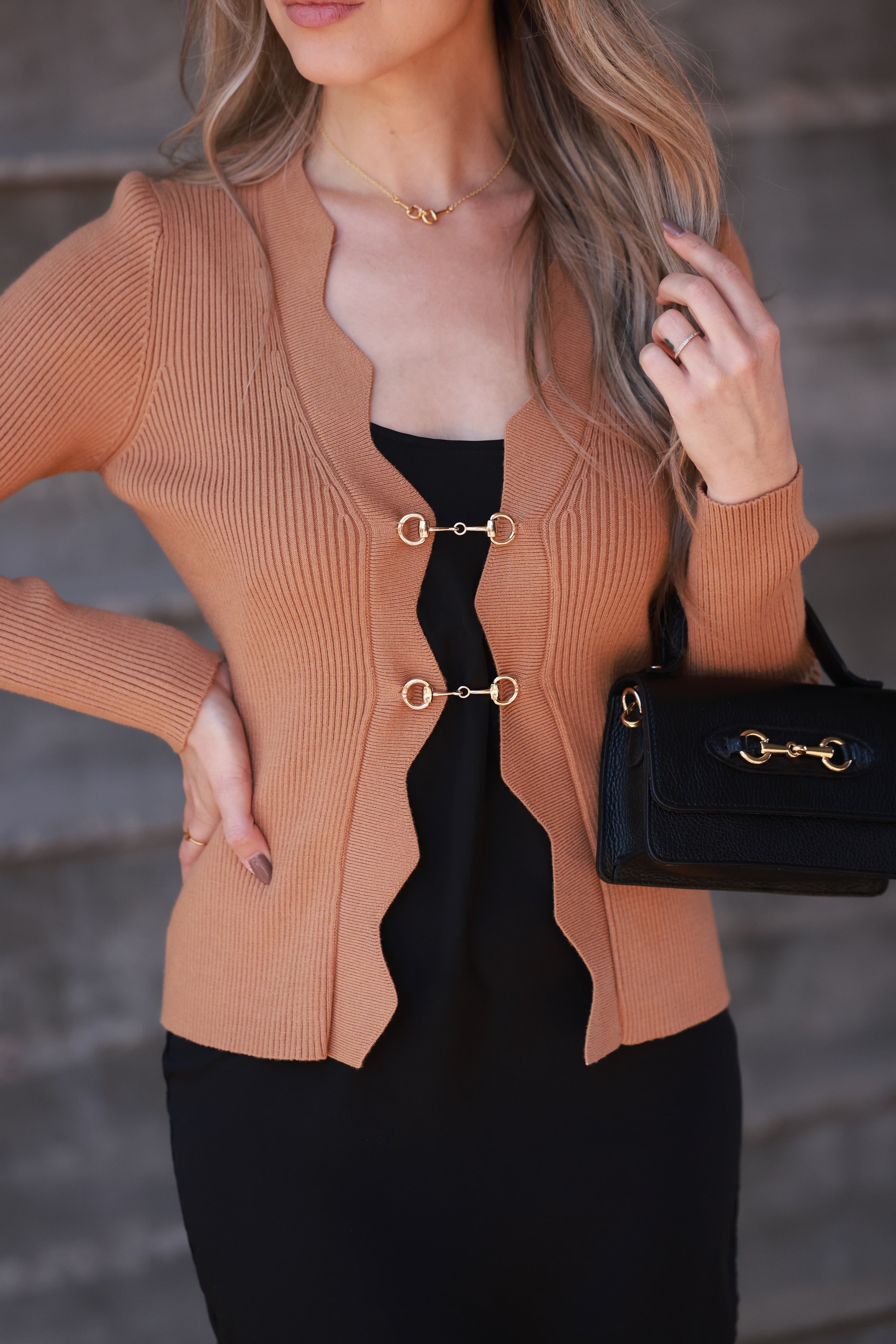 Camel-toned ribbed knit equestrian top featuring a deep scalloped neckline and two gold horsebit closures. Fitted long-sleeve cardigan-style top crafted from a poly/nylon blend, combining timeless elegance with refined equestrian detailing—perfect for fall and winter equestrian fashion.