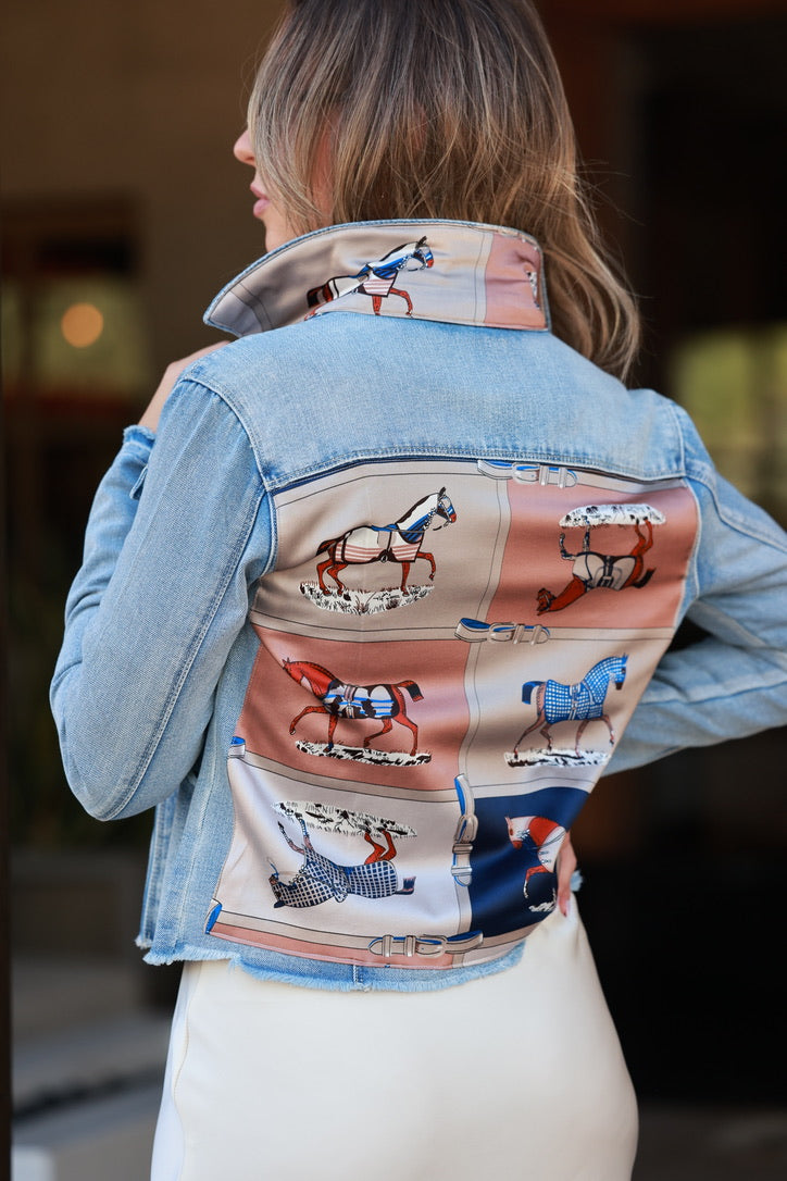 Person wearing a denim jacket with a colorful back panel featuring horse illustrations. - equestrian apparel, horse print jean jacket, horse motif scarf pattern, horse girl apparel