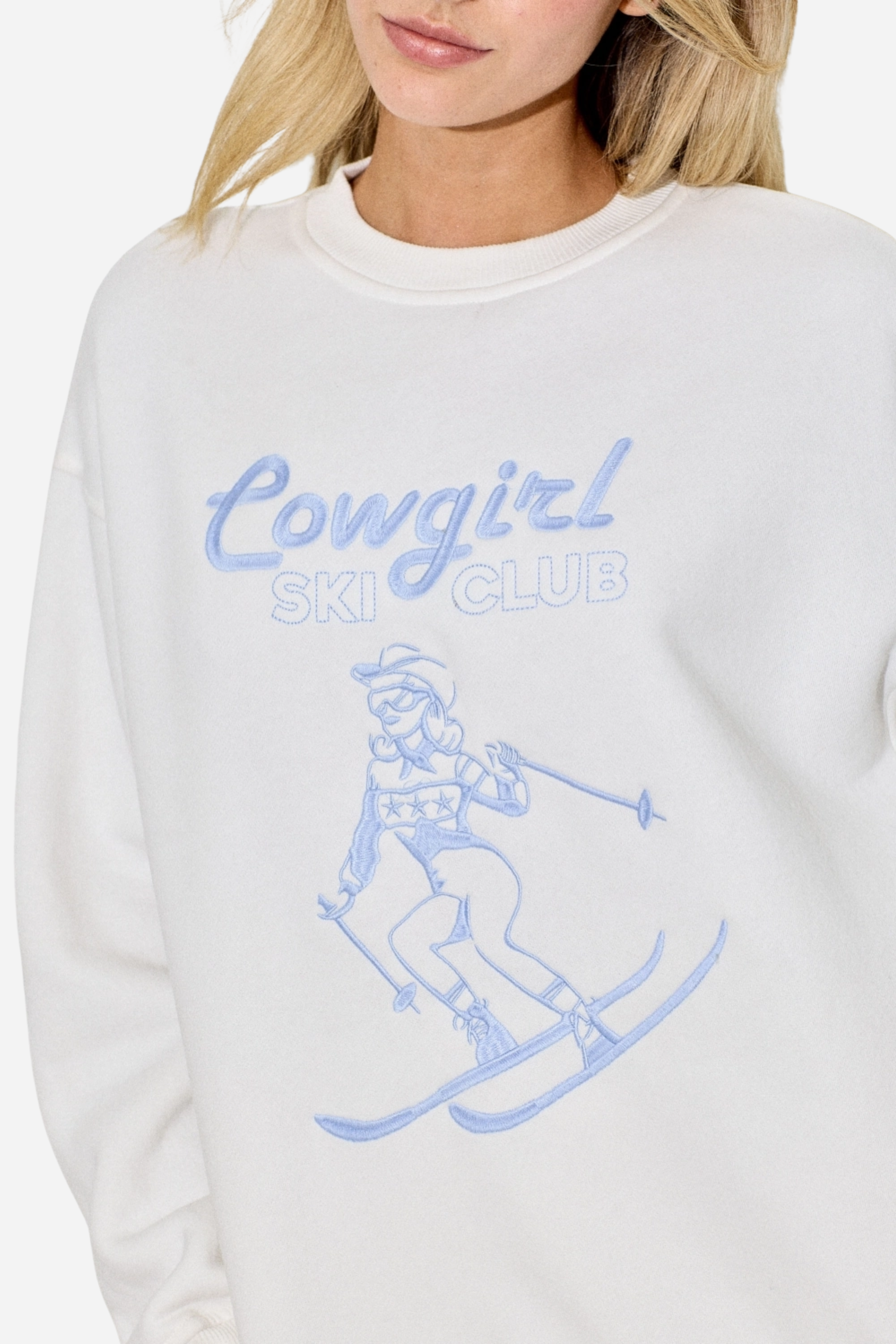 Cowgirl Ski Club Embroidered Sweatshirt — a cozy fleece pullover blending western charm with après-ski flair. Features a powder-blue embroidered skiing cowgirl graphic on soft cotton/poly fabric with ribbed cuffs, neckline, and hem. Relaxed fit for ultimate comfort and style, perfect for horse girls and western fashion lovers. western cowgirl embroidery detail, horse girl apparel, equestrian clothing, western riding sweatshirt, skiing cowgirl sweatshirt, cozy fleece pullover