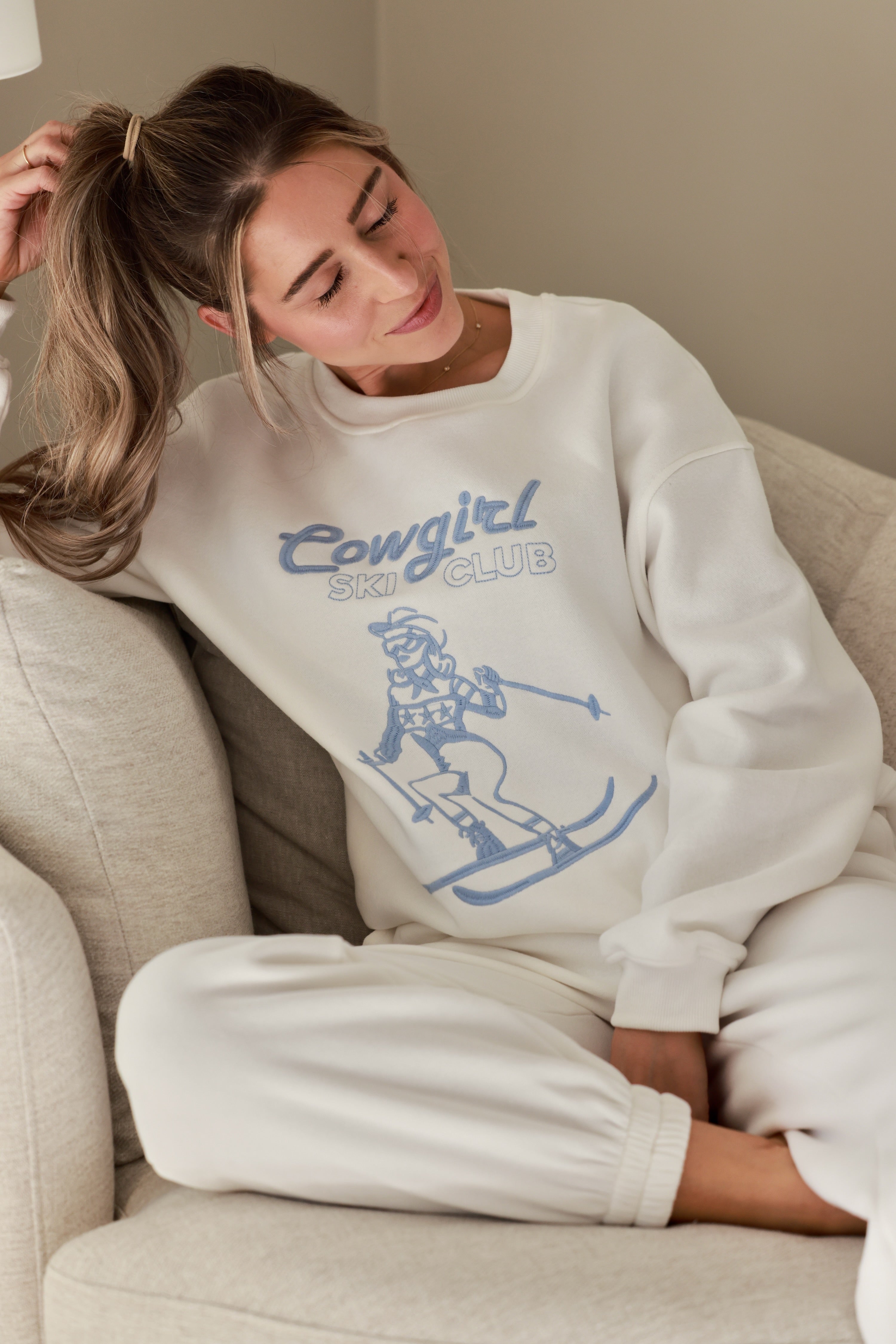 Cowgirl Ski Club Embroidered Sweatshirt — a cozy fleece pullover blending western charm with après-ski flair. Features a powder-blue embroidered skiing cowgirl graphic on soft cotton/poly fabric with ribbed cuffs, neckline, and hem. Relaxed fit for ultimate comfort and style, perfect for horse girls and western fashion lovers. western cowgirl embroidery detail, horse girl apparel, equestrian clothing, western riding sweatshirt, skiing cowgirl sweatshirt, cozy fleece pullover