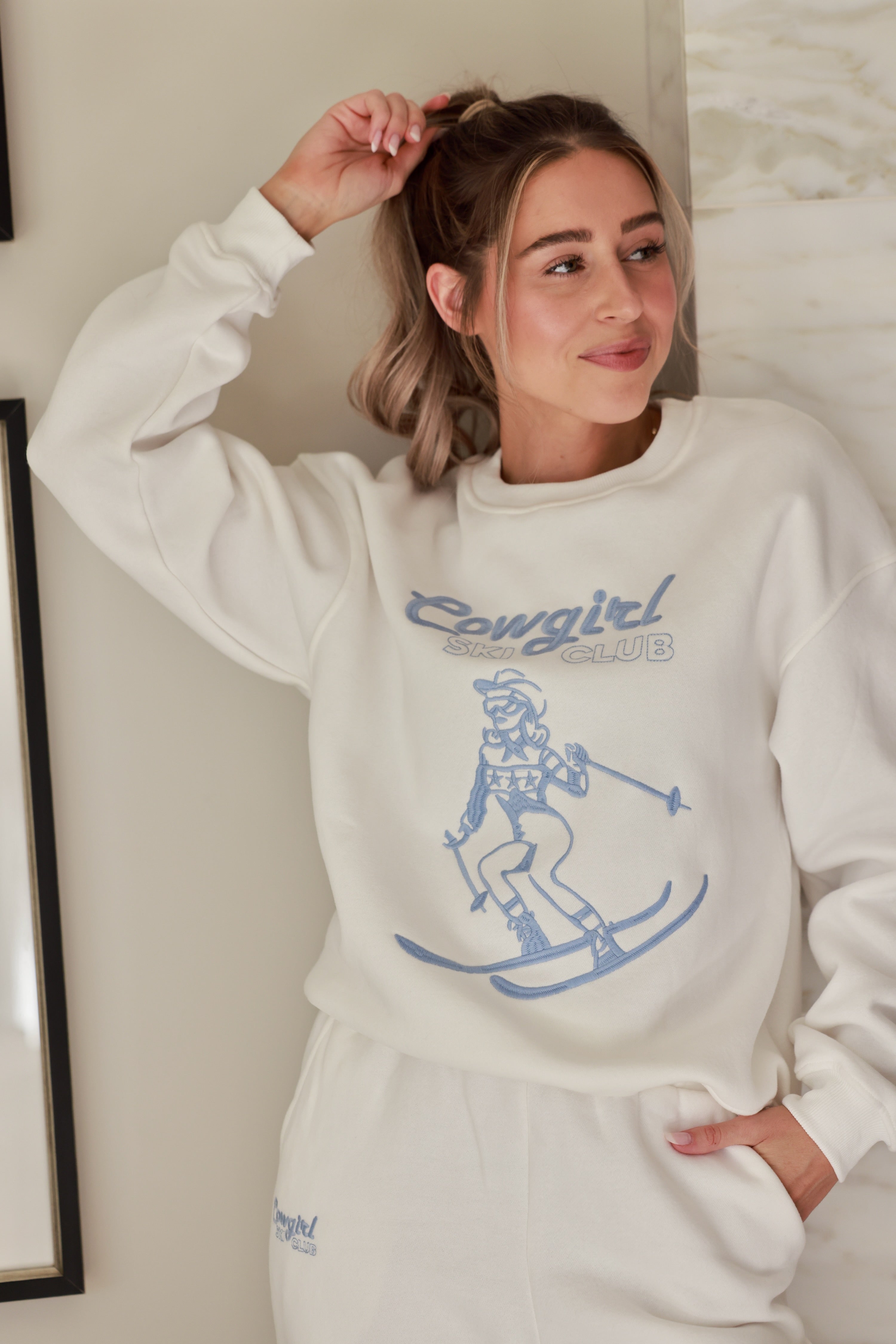 Cowgirl Ski Club Embroidered Sweatshirt — a cozy fleece pullover blending western charm with après-ski flair. Features a powder-blue embroidered skiing cowgirl graphic on soft cotton/poly fabric with ribbed cuffs, neckline, and hem. Relaxed fit for ultimate comfort and style, perfect for horse girls and western fashion lovers. western cowgirl embroidery detail, horse girl apparel, equestrian clothing, western riding sweatshirt, skiing cowgirl sweatshirt, cozy fleece pullover