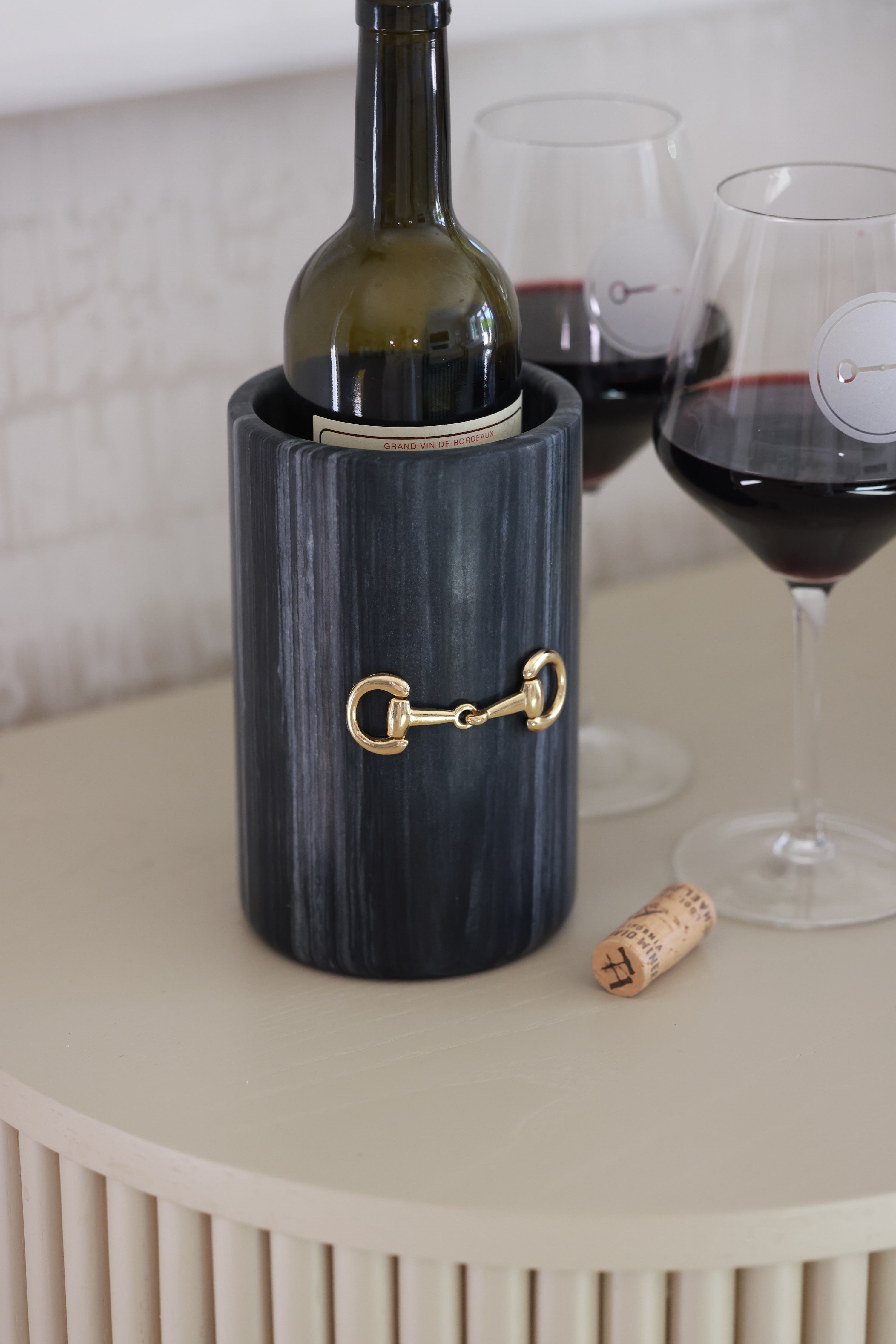 Handcrafted black marble D-ring cylinder with polished gold horse bit hardware, styled in an elegant equestrian kitchen. The sleek matte marble vessel doubles as a wine chiller, utensil holder, or flower vase, featuring natural veining and timeless horse-inspired detailing for a sophisticated home accent.