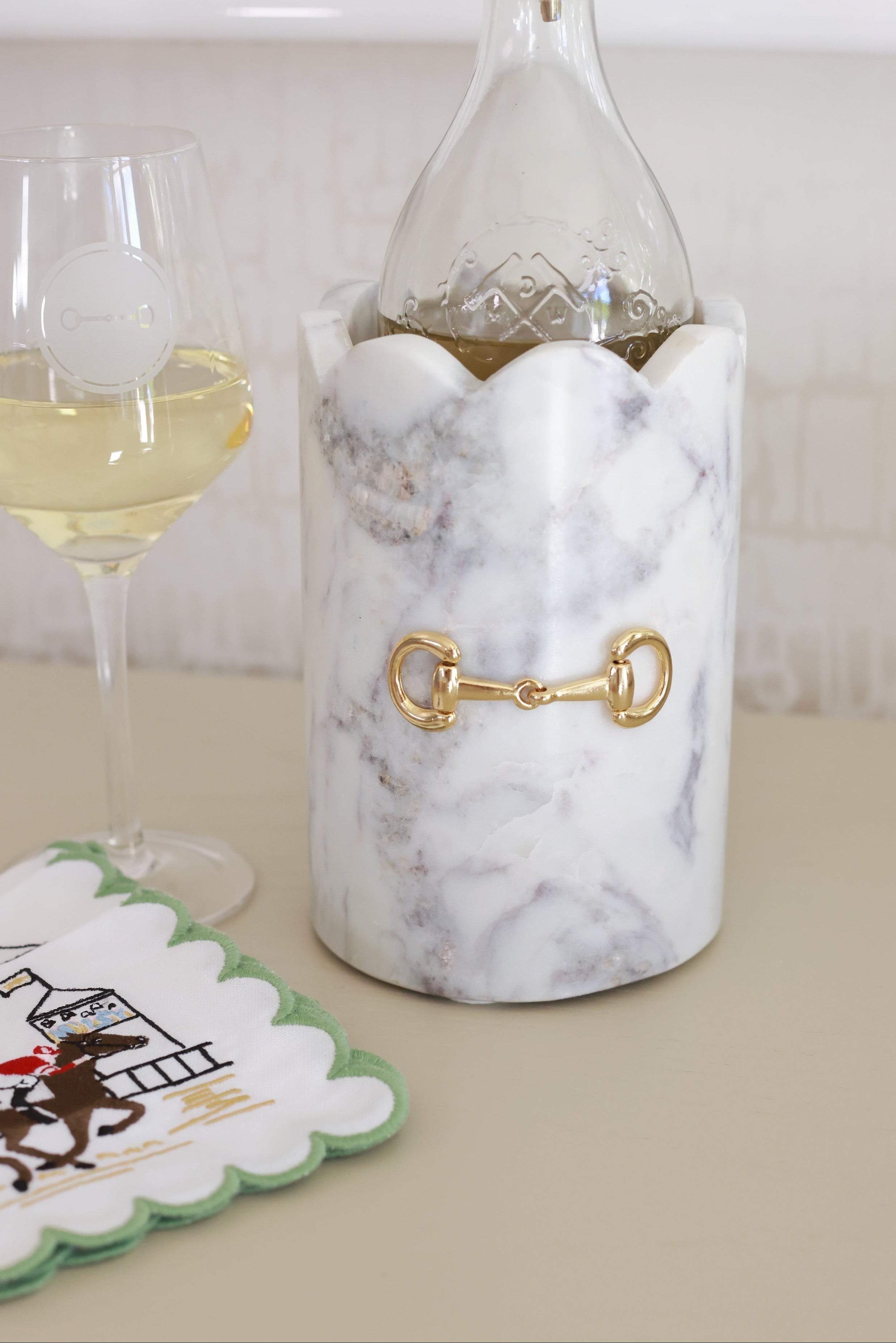 Luxurious white marble D-ring scalloped wine chiller with polished gold horse bit hardware, handcrafted for an elegant equestrian-inspired home. The cylindrical marble design features subtle natural veining, perfect for chilling wine or champagne, or as a stylish horse-themed vase or utensil holder.