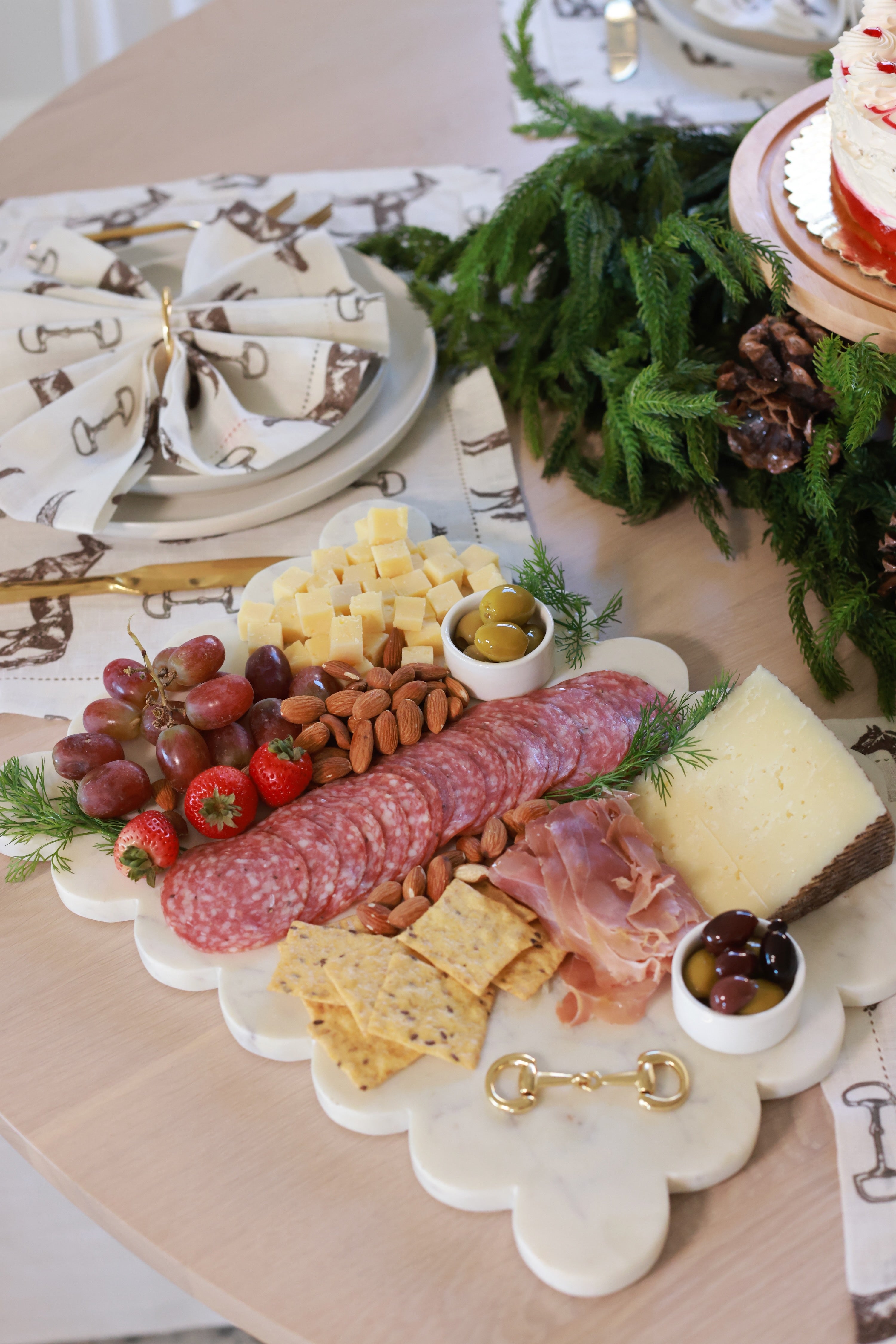 Elegant white marble scalloped serving board with gold D-ring bit, styled in an equestrian-themed kitchen. The handcrafted marble board features subtle natural veining and polished gold hardware, displayed with cheese, fruits, and wine accents. Perfect as a horse-inspired charcuterie tray or decorative equestrian home accent.