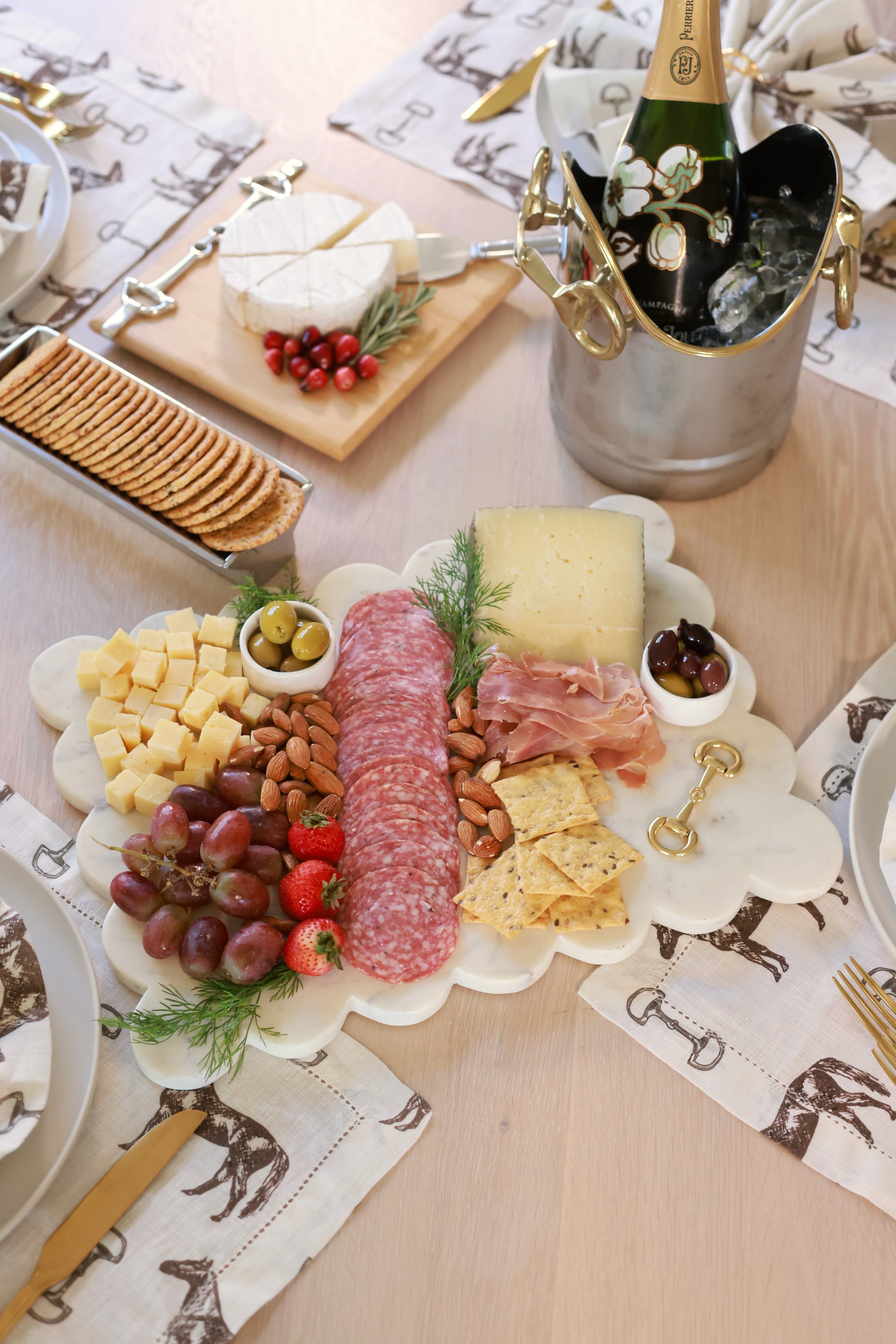 Elegant white marble scalloped serving board with gold D-ring bit, styled in an equestrian-themed kitchen. The handcrafted marble board features subtle natural veining and polished gold hardware, displayed with cheese, fruits, and wine accents. Perfect as a horse-inspired charcuterie tray or decorative equestrian home accent.