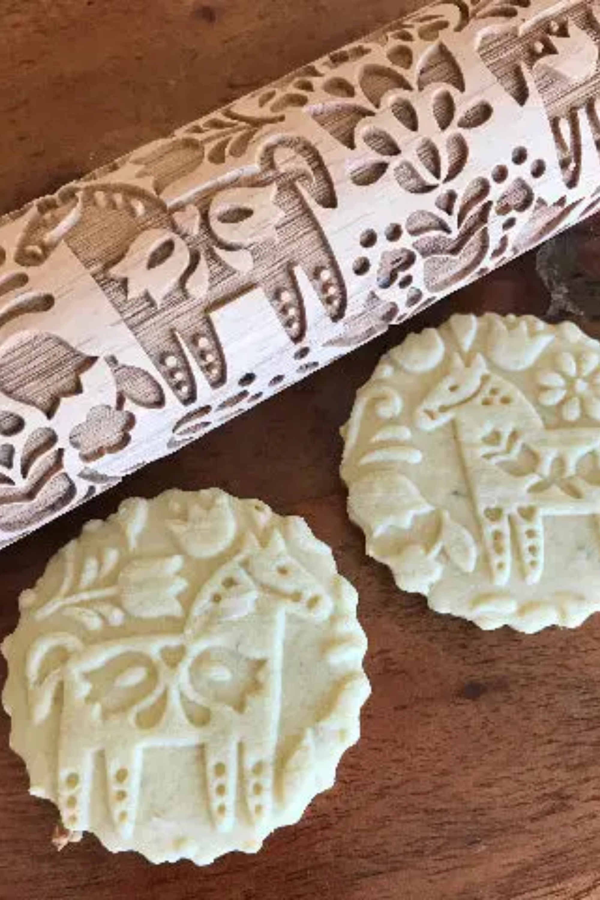 A Dala Horse Embossed Rolling Pin with an intricate floral pattern carved into its surface, designed for imprinting elegant Swedish-inspired motifs onto cookie dough, fondant, or craft materials. The rolling pin rests on a light wooden surface beside freshly embossed cookies and baking ingredients, showcasing its detailed craftsmanship and versatility for baking and crafting projects.