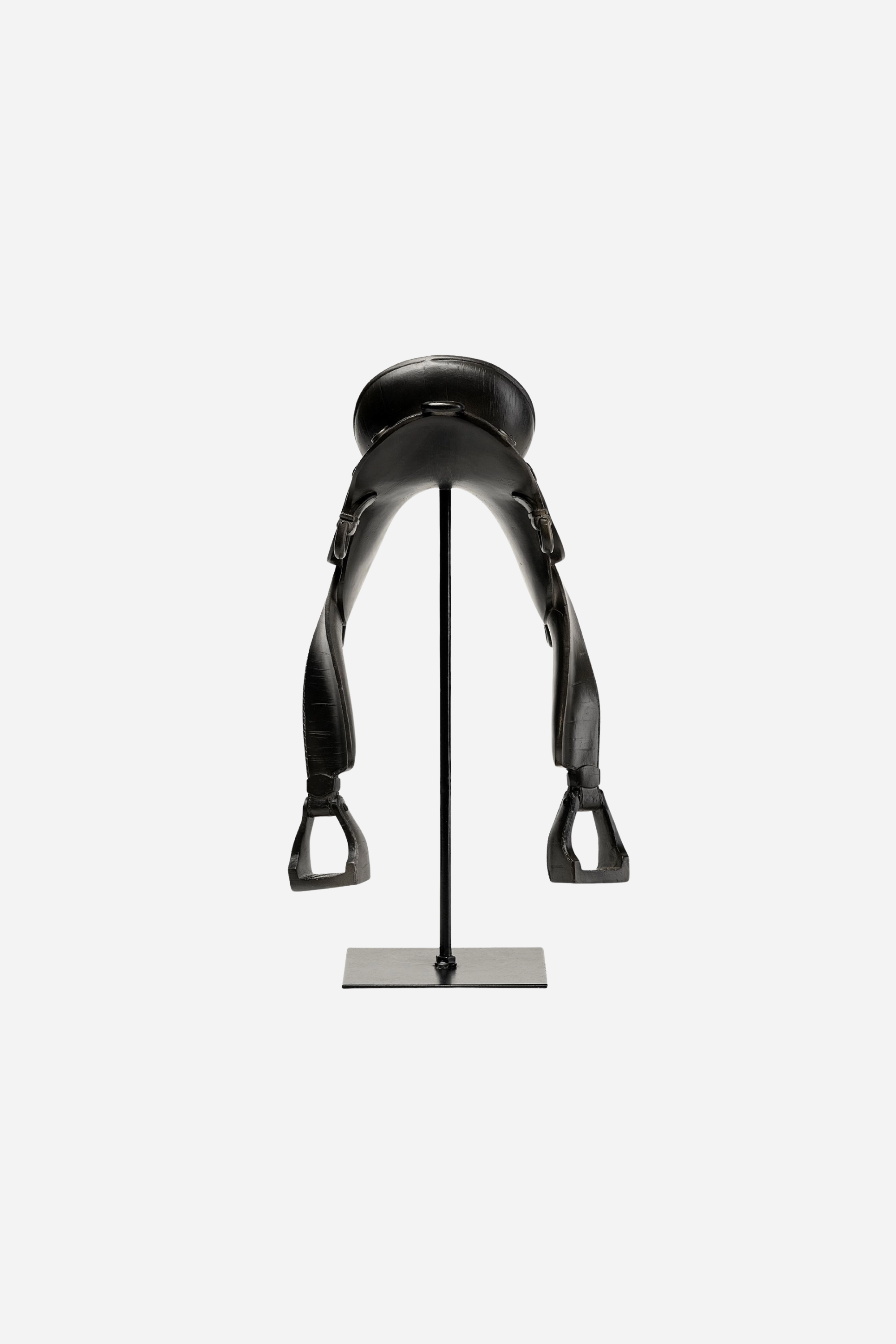 A matte black English-style equestrian saddle decor piece crafted from resin and metal, featuring fine detailing that mimics real saddle stitching and hardware. The saddle sits atop a sleek black metal rod and square base, standing 17 inches tall. Its minimalist, modern design evokes traditional riding gear while serving as a bold centerpiece for equestrian-themed home decor.
