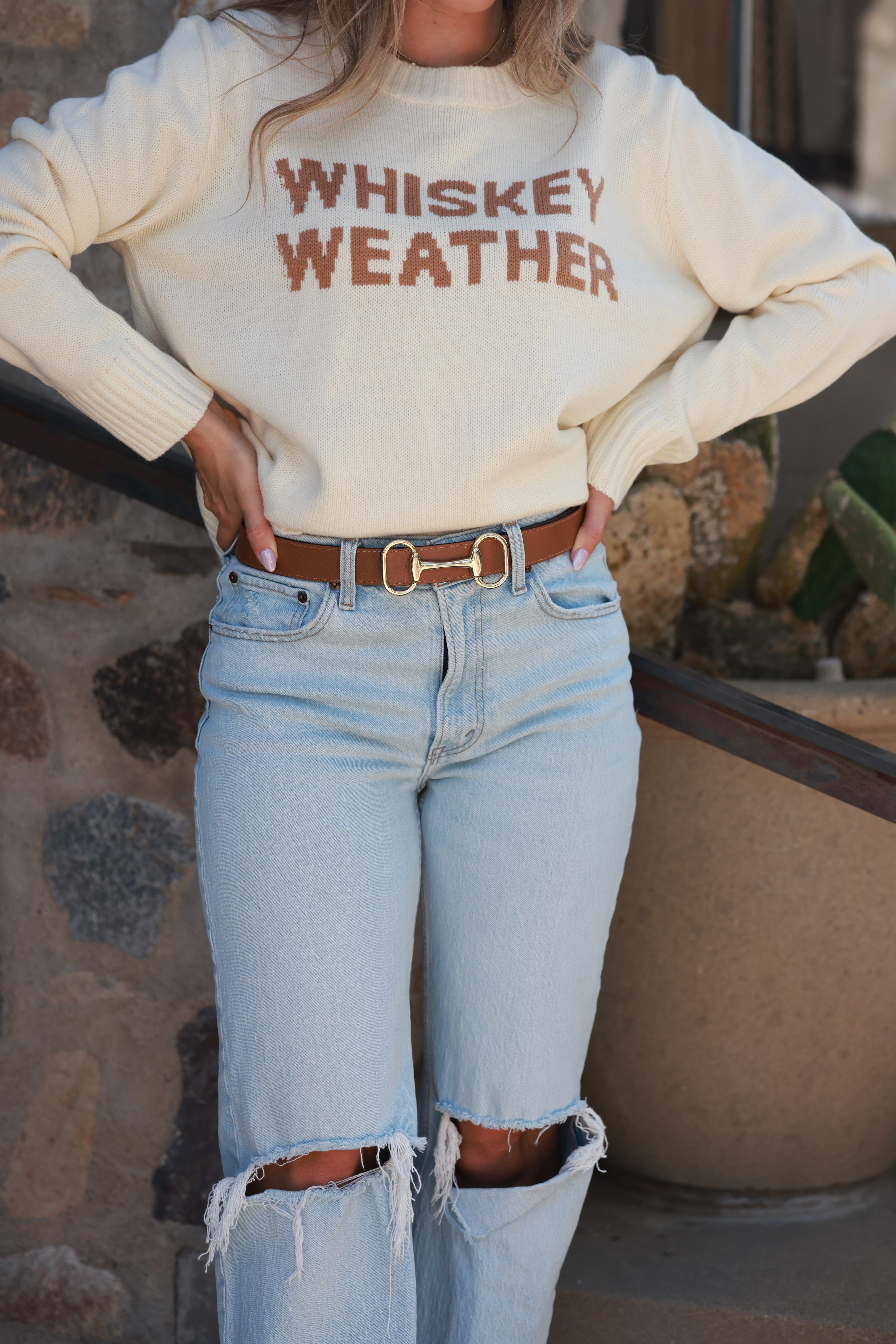 Person wearing a cream sweatshirt with 'WHISKEY WEATHER' text and light blue jeans. - equestrian accessory, horse themed belt, horse bit leather belt, accessories for horse girls