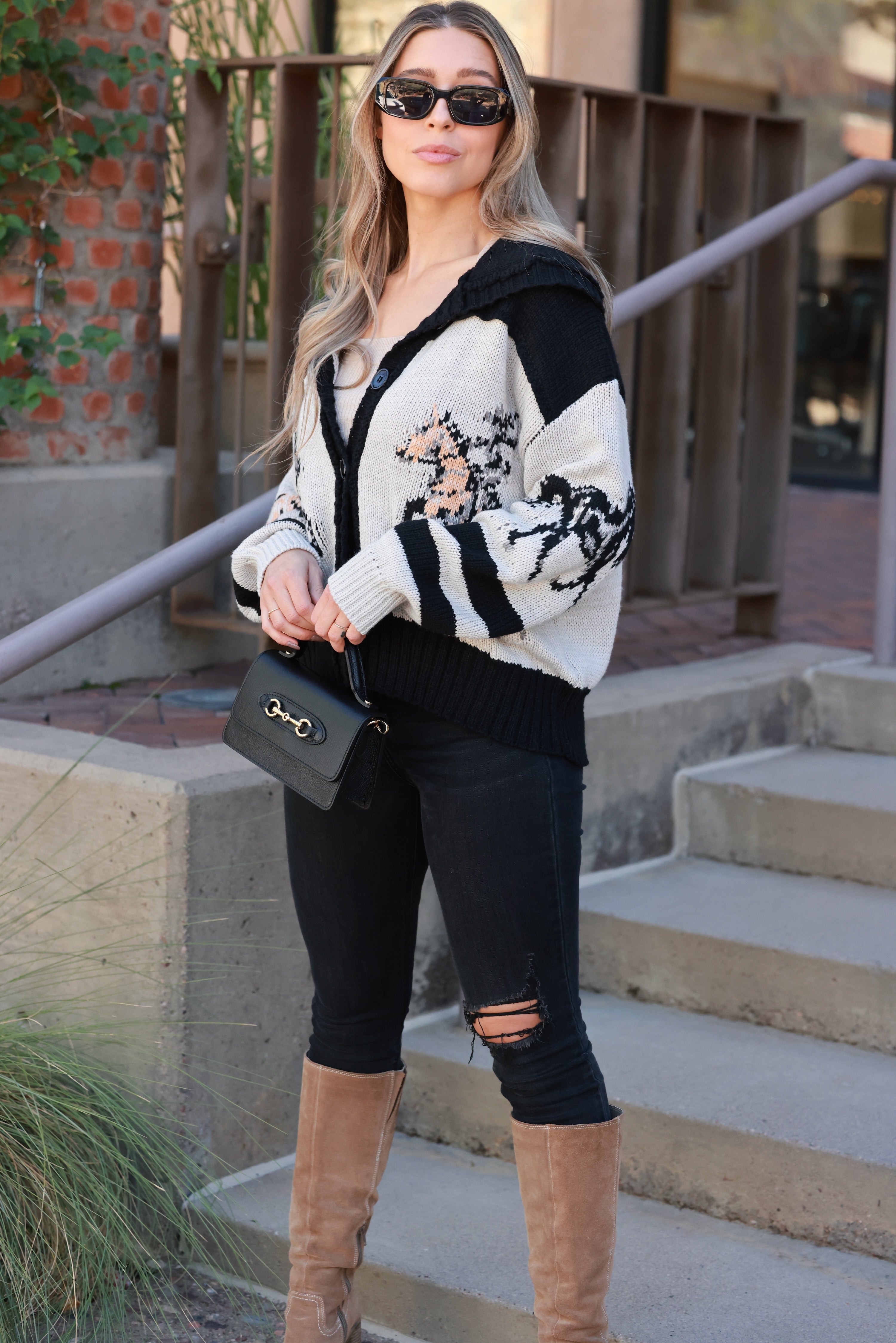 Chunky knit button-down cardigan featuring galloping horse patterns across the front, sleeves, and back. Designed with bold varsity-style stripes, a fold-over collar, and a relaxed oversized fit for cozy equestrian-inspired style.