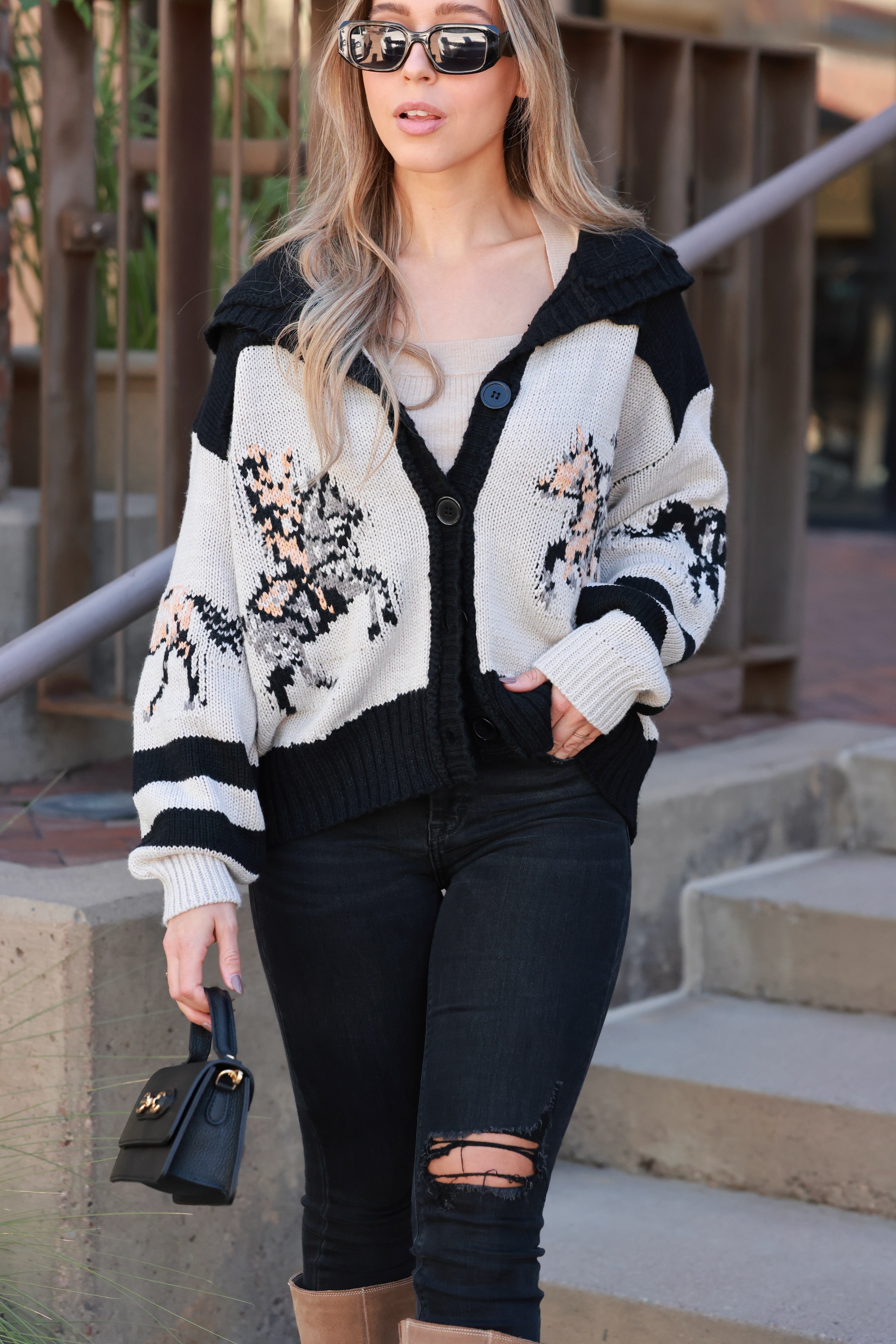 Chunky knit button-down cardigan featuring galloping horse patterns across the front, sleeves, and back. Designed with bold varsity-style stripes, a fold-over collar, and a relaxed oversized fit for cozy equestrian-inspired style.