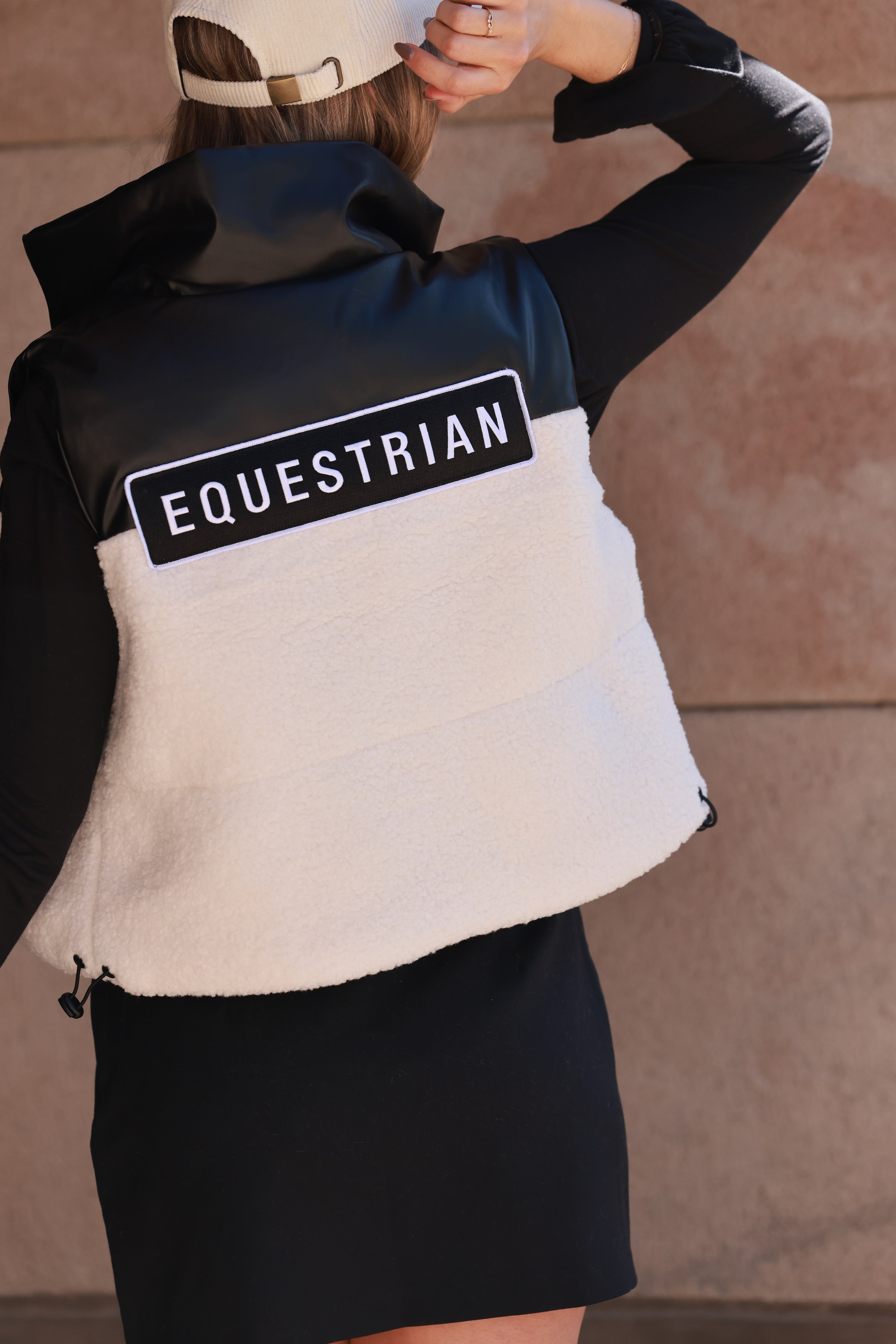 Stylish equestrian cropped puffer vest featuring contrasting sherpa and faux leather panels, embroidered equestrian patch on back, full zip front, and interior drawstring for a flattering fit — the ultimate trendy horse girl winter vest.