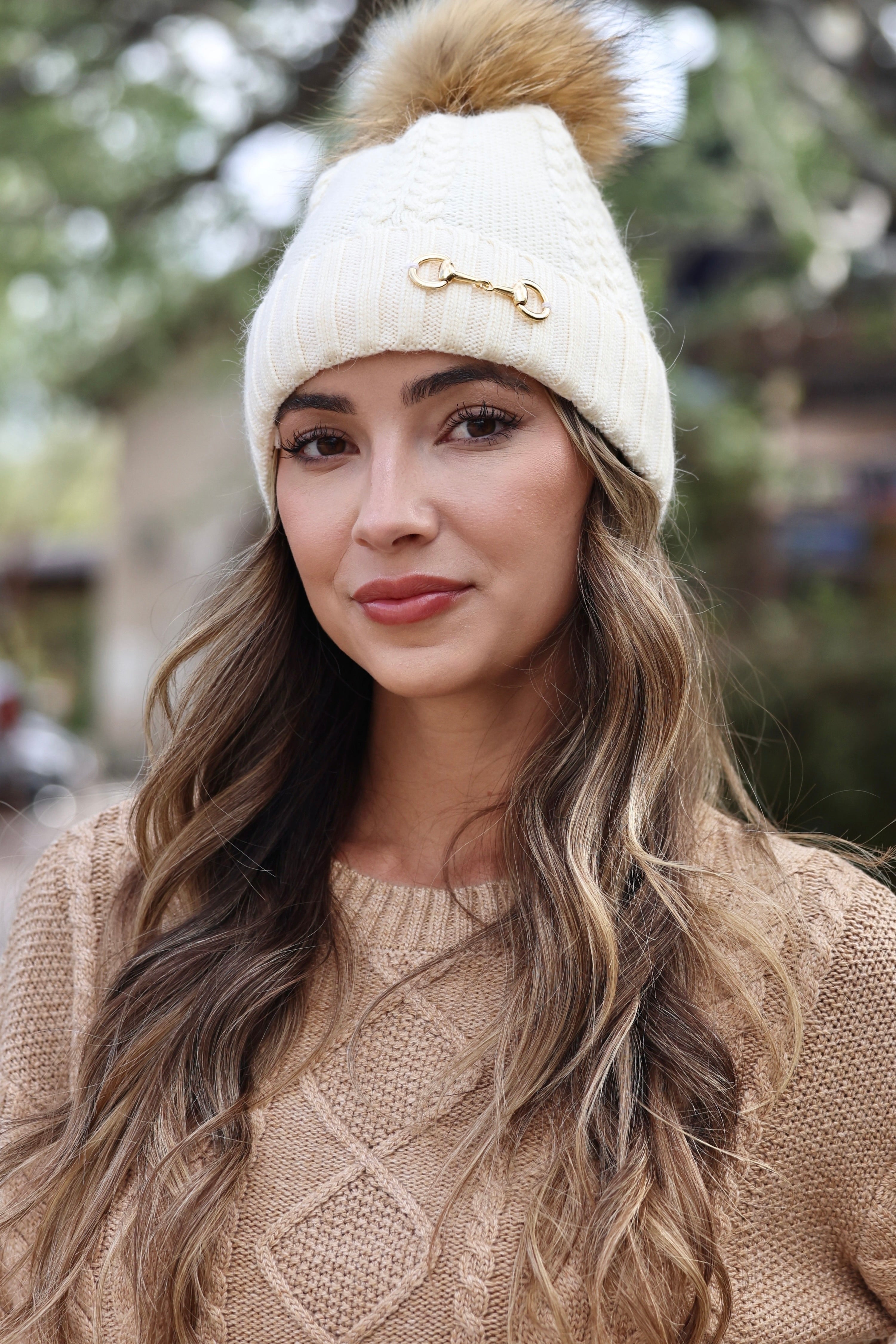 Ivory Evie Beanie featuring a soft, cozy medium-knit cable design with a polished gold bit accent and removable faux fur pom. A timeless equestrian winter accessory that blends warmth with chic style.