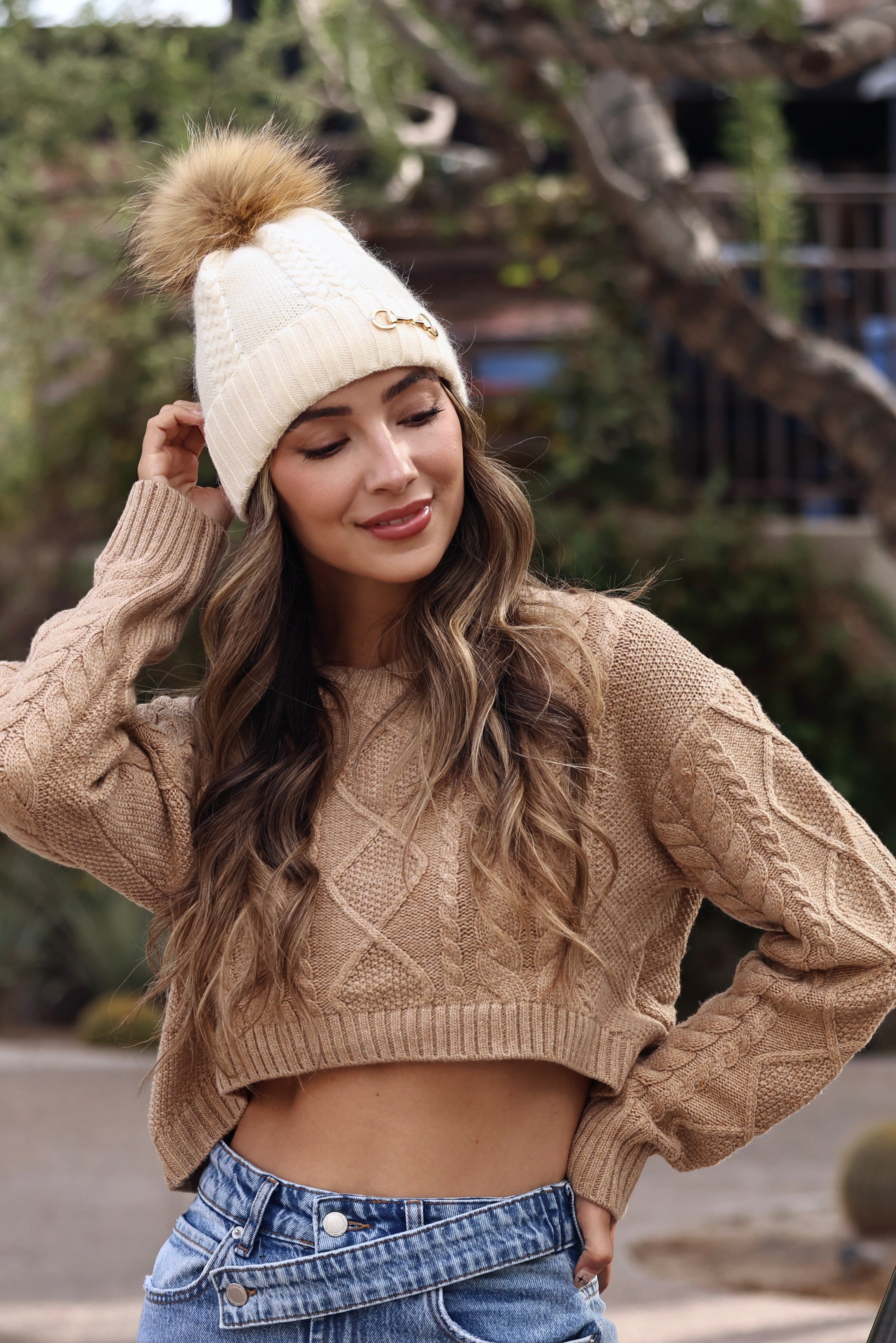 Ivory Evie Beanie featuring a soft, cozy medium-knit cable design with a polished gold bit accent and removable faux fur pom. A timeless equestrian winter accessory that blends warmth with chic style.