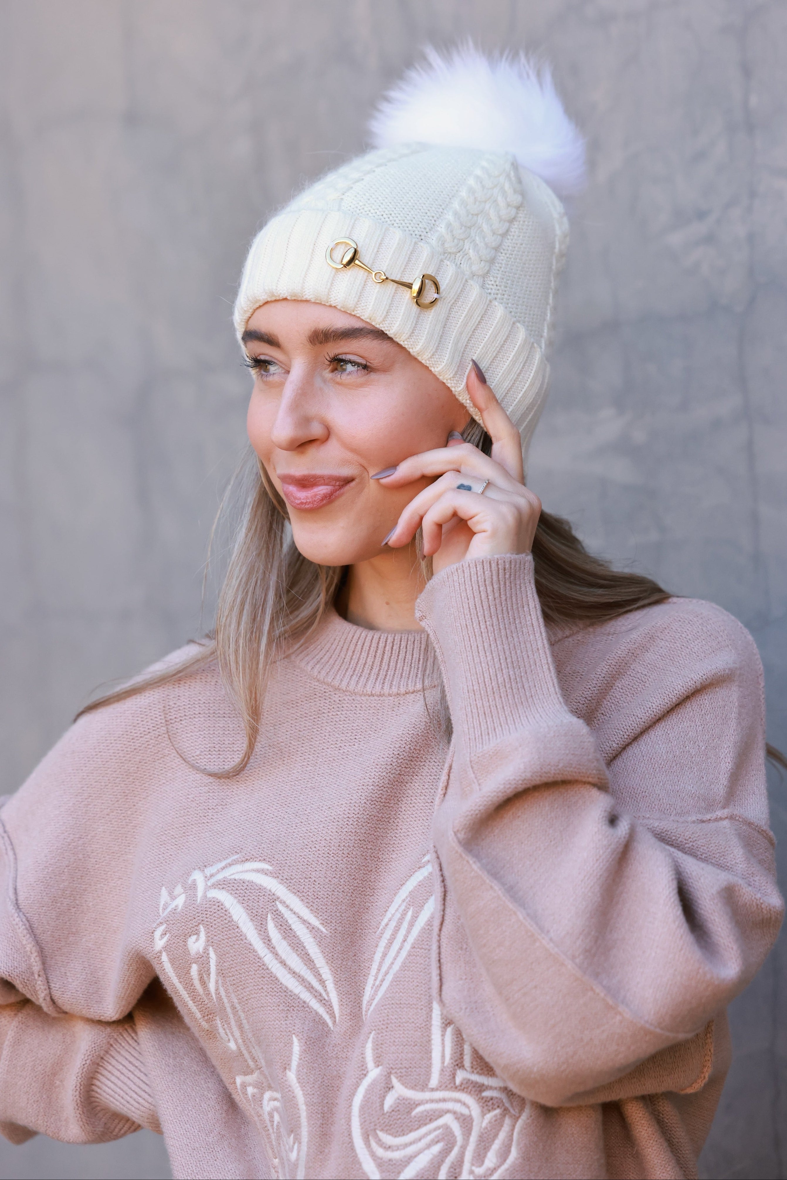 Ivory Evie Beanie featuring a soft, cozy medium-knit cable design with a polished gold bit accent and removable faux fur pom. A timeless equestrian winter accessory that blends warmth with chic style.