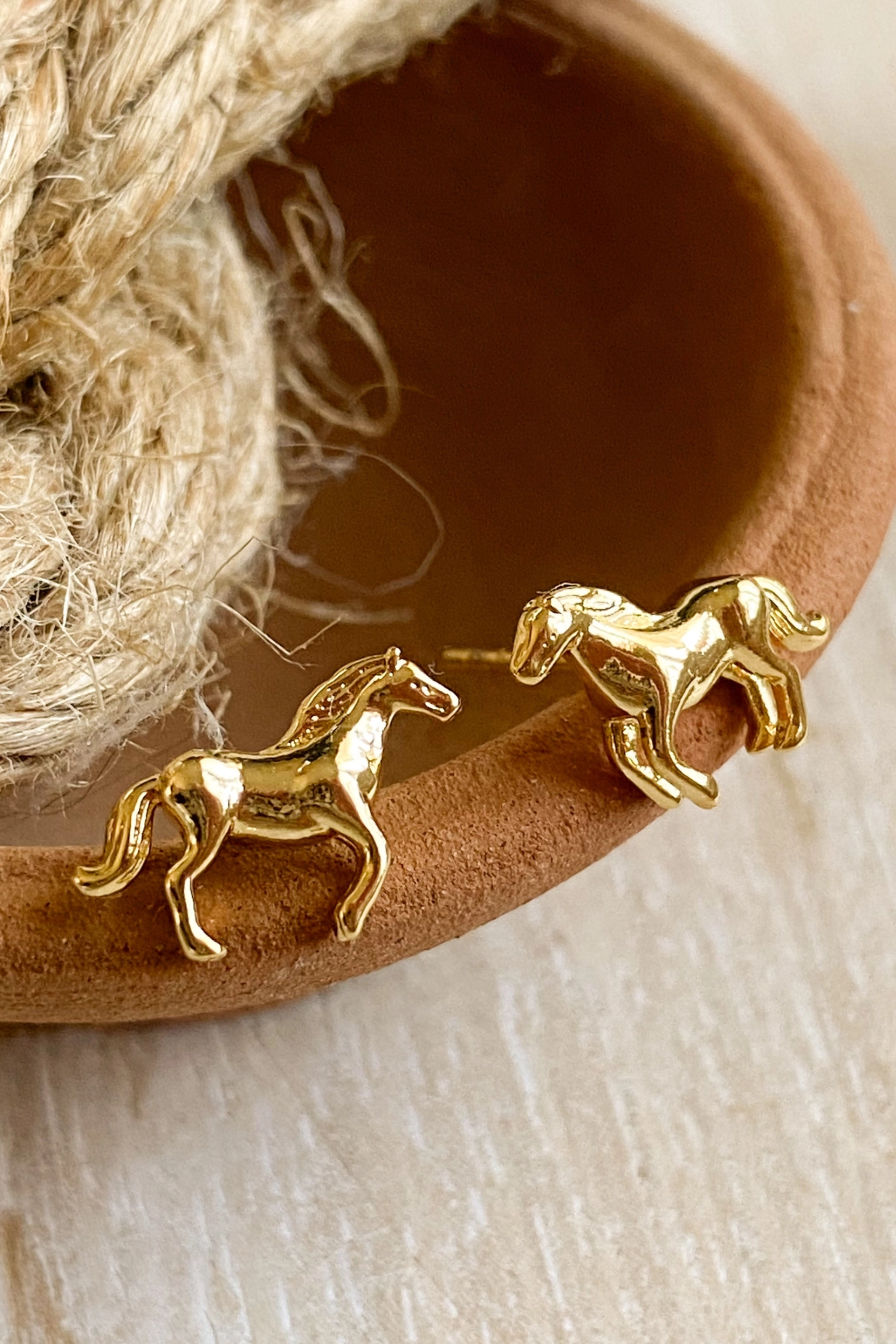 Pair of dainty gold horse-shaped stud earrings displayed on a white background, their detailed mane and tail catching the light for an elegant look. Made with 14K gold plating and nickel-free, perfect for horse lovers and equestrian enthusiasts.