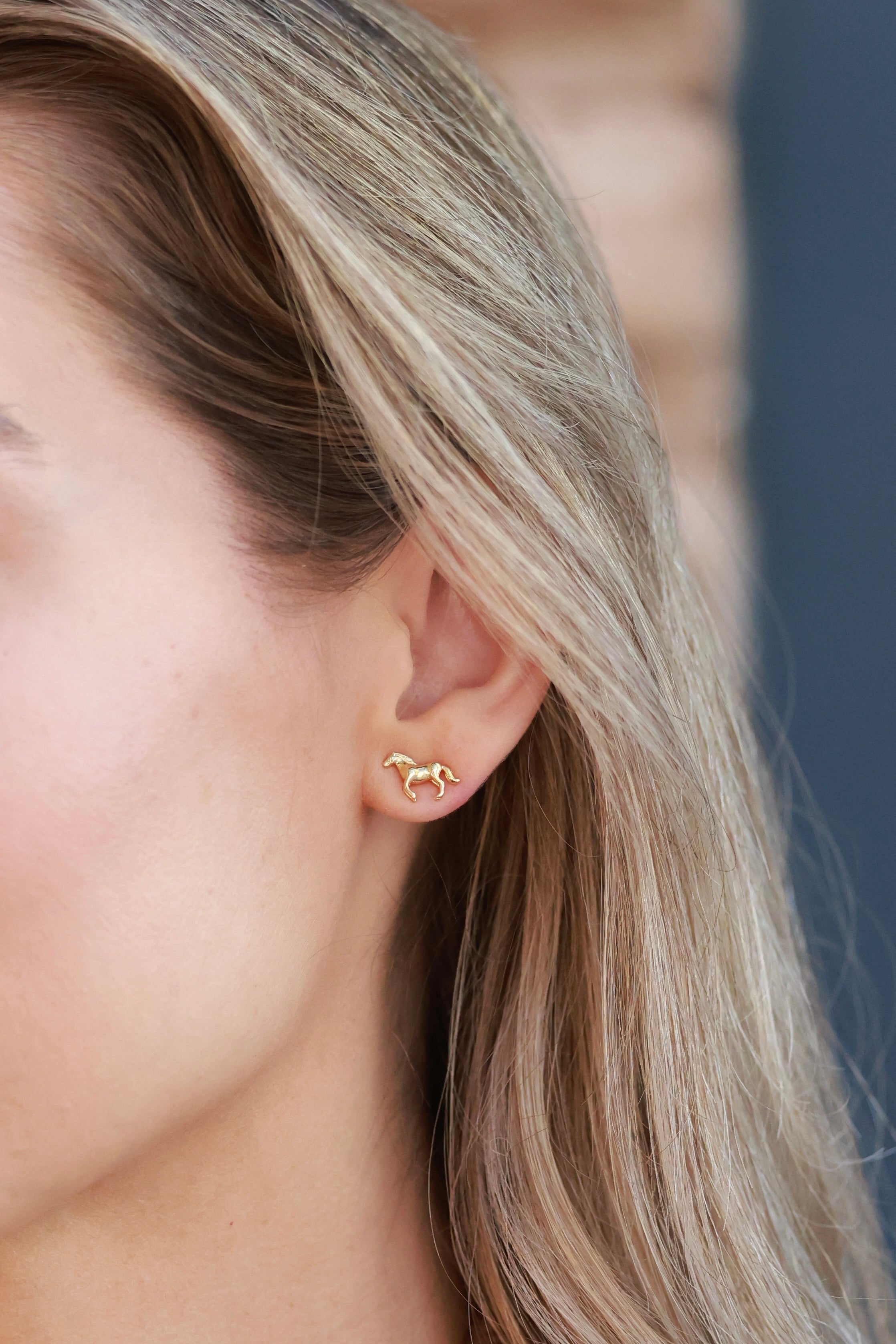 Pair of dainty gold horse-shaped stud earrings displayed on a white background, their detailed mane and tail catching the light for an elegant look. Made with 14K gold plating and nickel-free, perfect for horse lovers and equestrian enthusiasts.