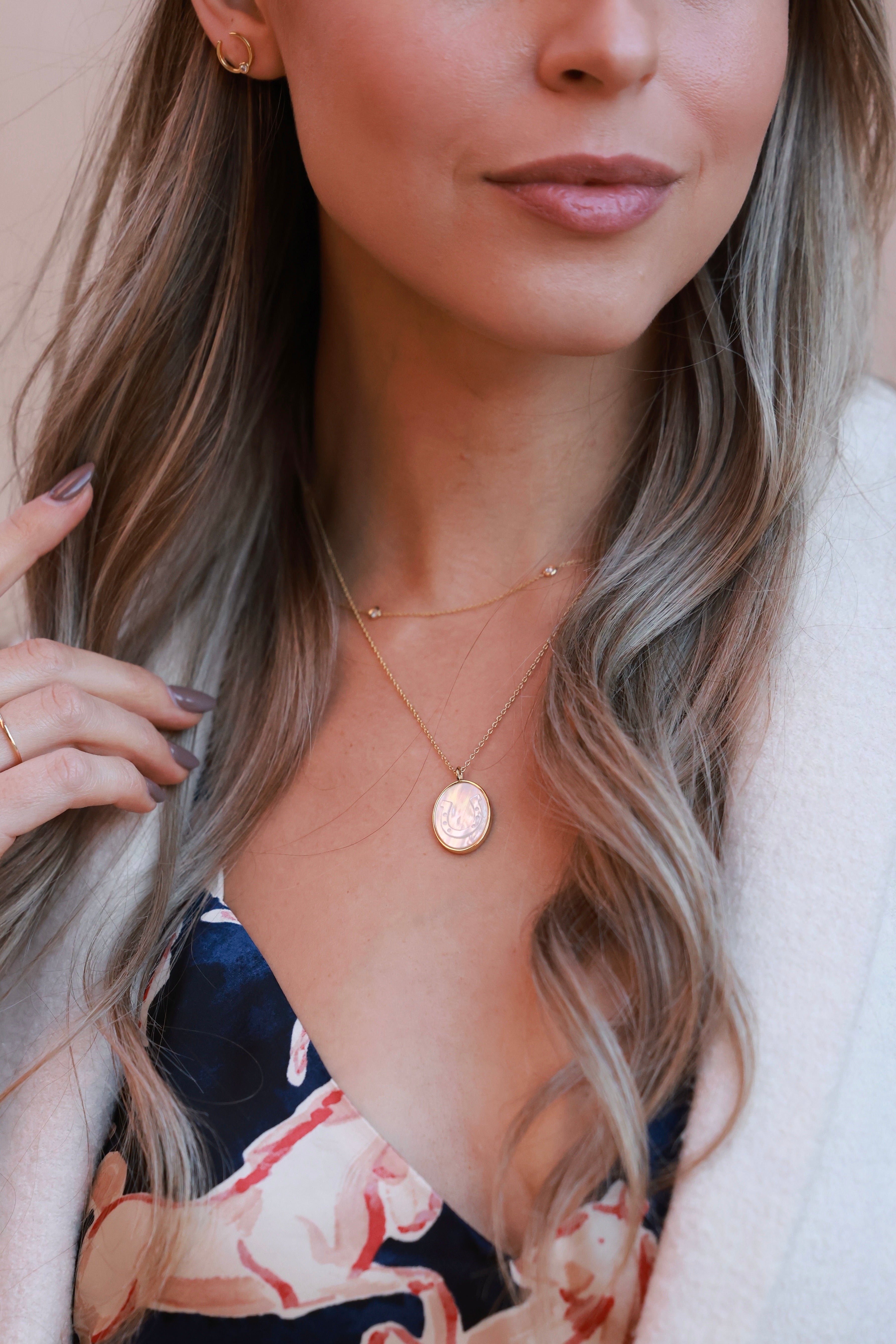 Lucky Cowgirl Necklace featuring a delicate gold-framed pendant with an intricately etched horseshoe design set in luminous mother-of-pearl. 18-inch plated brass chain with .95-inch pendant — a dainty equestrian-inspired accessory perfect for horse lovers.