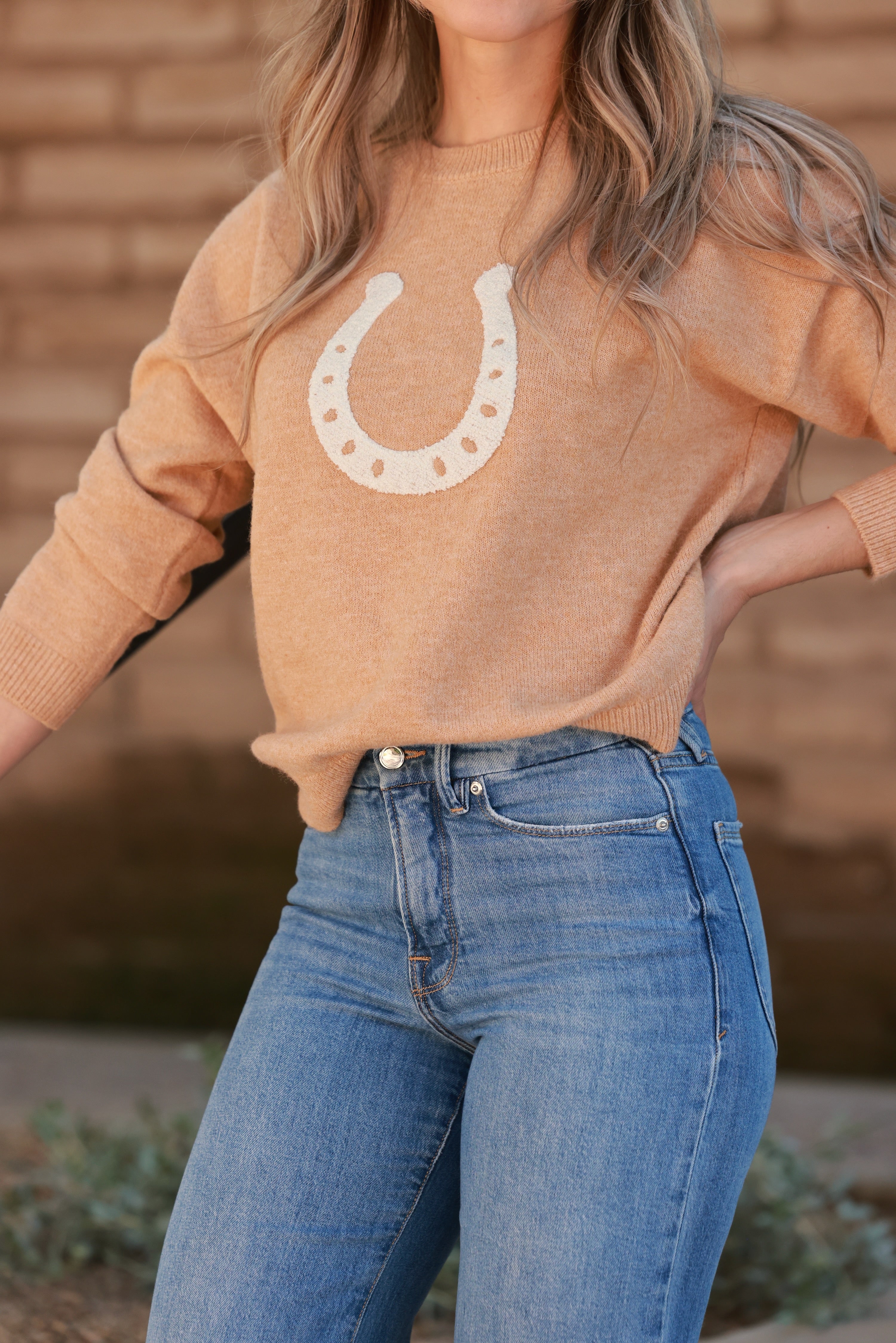 Lucky Daze Horseshoe Sweater in warm camel featuring a soft acrylic-nylon-poly knit with a fuzzy chenille horseshoe patch on the front. Slightly cropped fit with ribbed neckline, cuffs, and hem. A cozy equestrian-inspired crewneck supporting the Bridle Up Hope charity for women and girls.