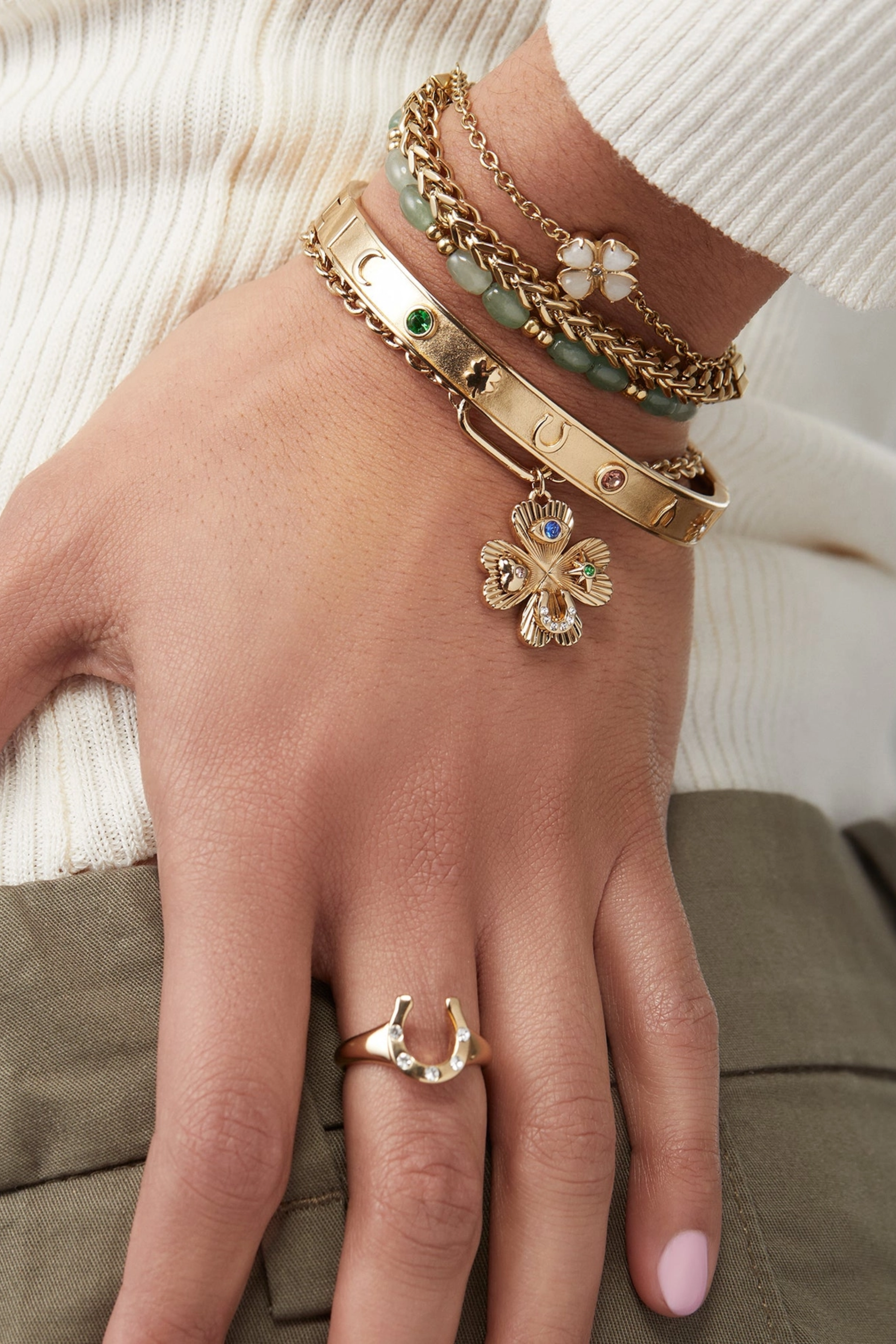 Gold hinge bangle bracelet featuring lucky charm symbols—horseshoe, wishbone, and four-leaf clover—accented with colored crystal details.