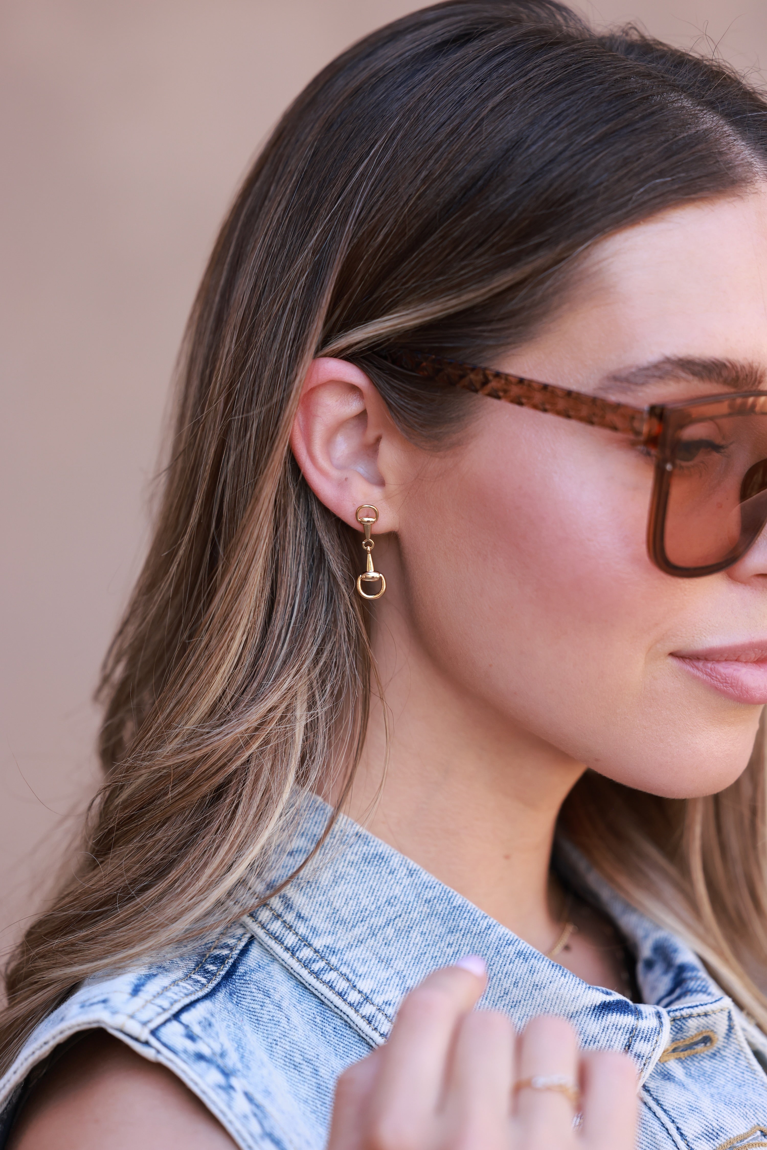 Close-up of a woman wearing sunglasses and a gold earring with a small lock charm. - horse bit earrings, equestrian inspired jewelry, horse bit jewelry, equestrian accessories, dainty equestrian jewelry, snaffle bit earrings, horse girl jewelry, horse girl accessory