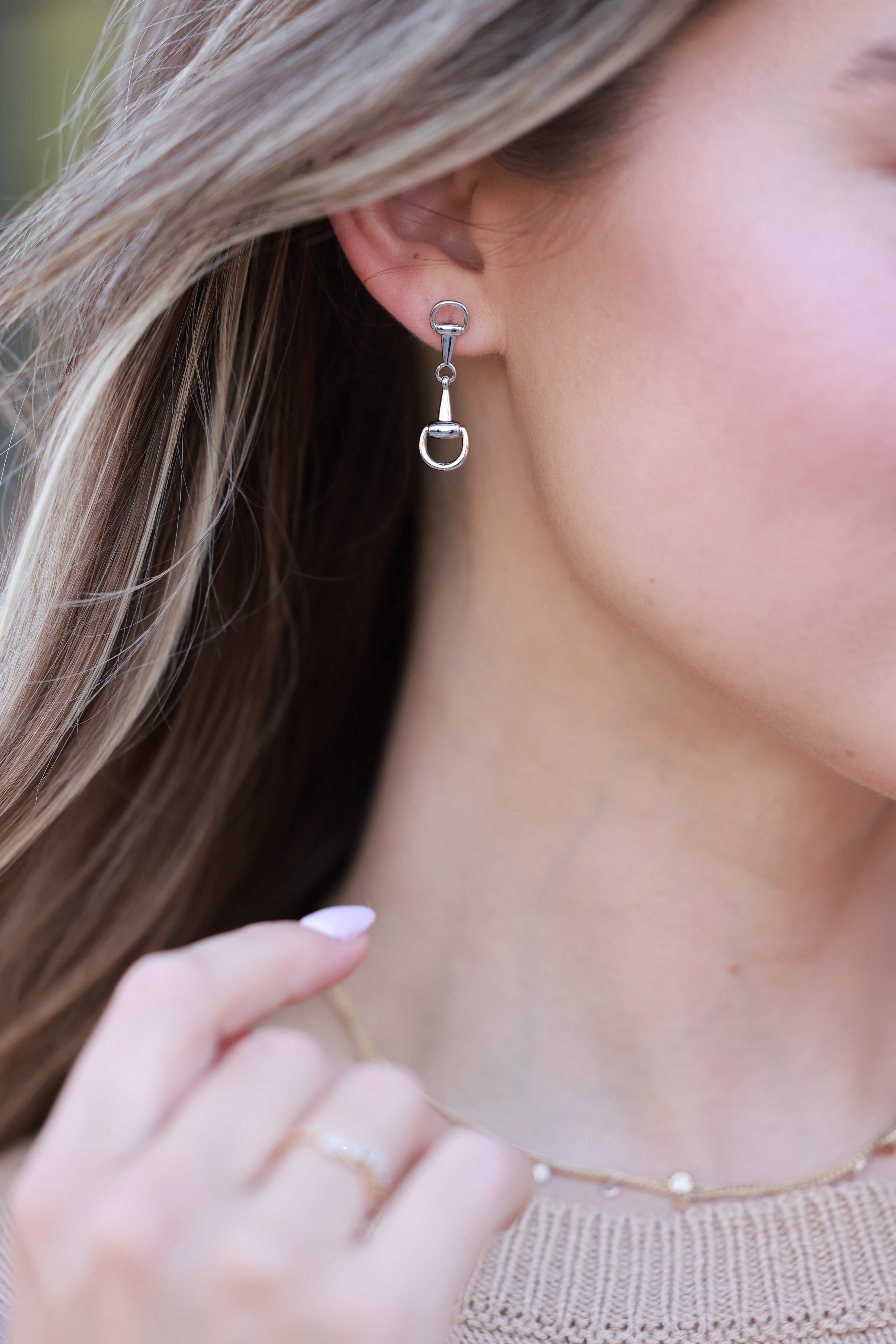 Close-up of a person wearing silver hoop earrings with a blurred - horse bit earrings, equestrian inspired jewelry, horse bit jewelry, equestrian accessories, dainty equestrian jewelry, snaffle bit earrings, horse girl jewelry, horse girl accessorybackground