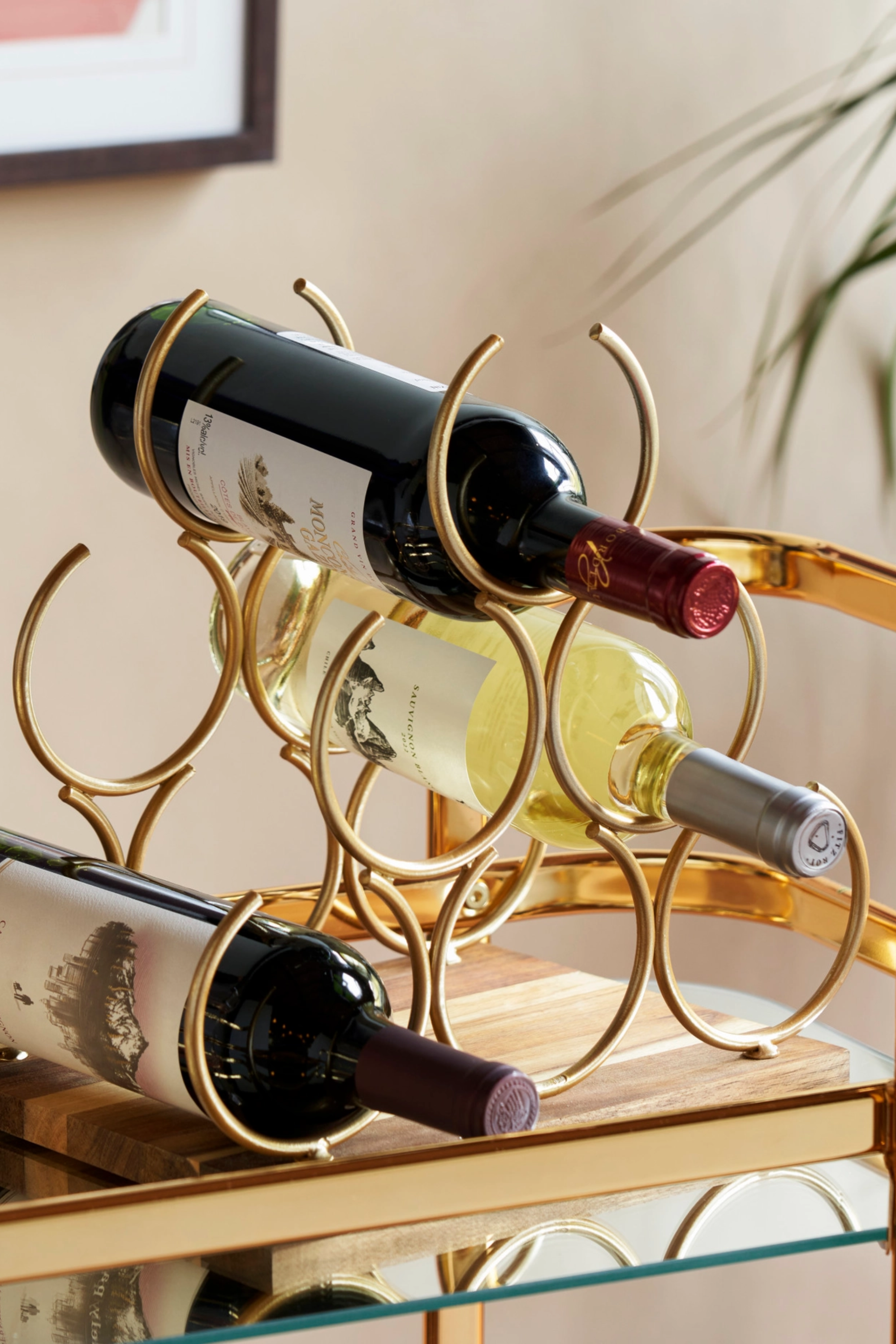 Gold metal geometric wine rack with a sleek, modern design, set on a natural acacia wood base. Measures 11.5'' high, 10.25'' wide, and 8.25'' deep, and holds up to six wine bottles, creating an elegant countertop display.