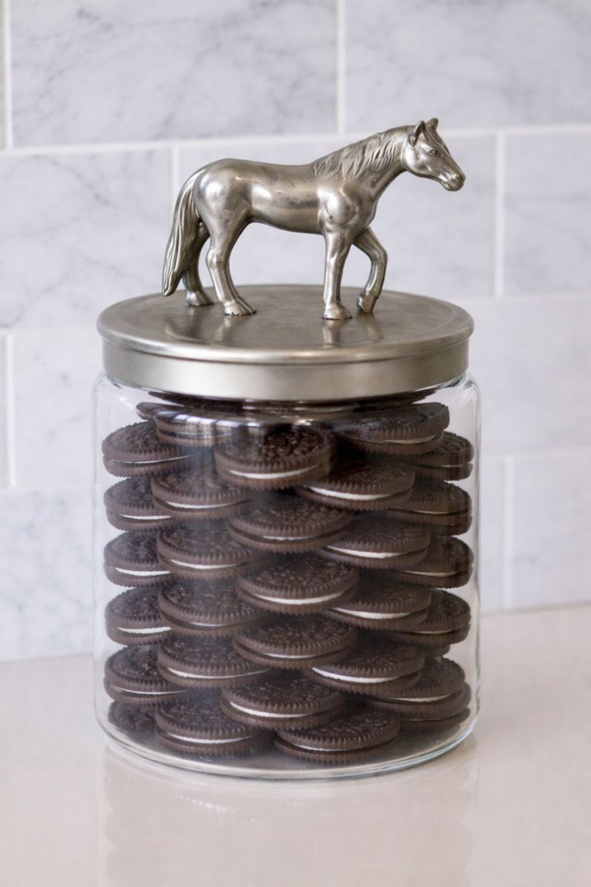 Clear glass storage jar with a brushed silver aluminum lid featuring a sculpted horse accent.
