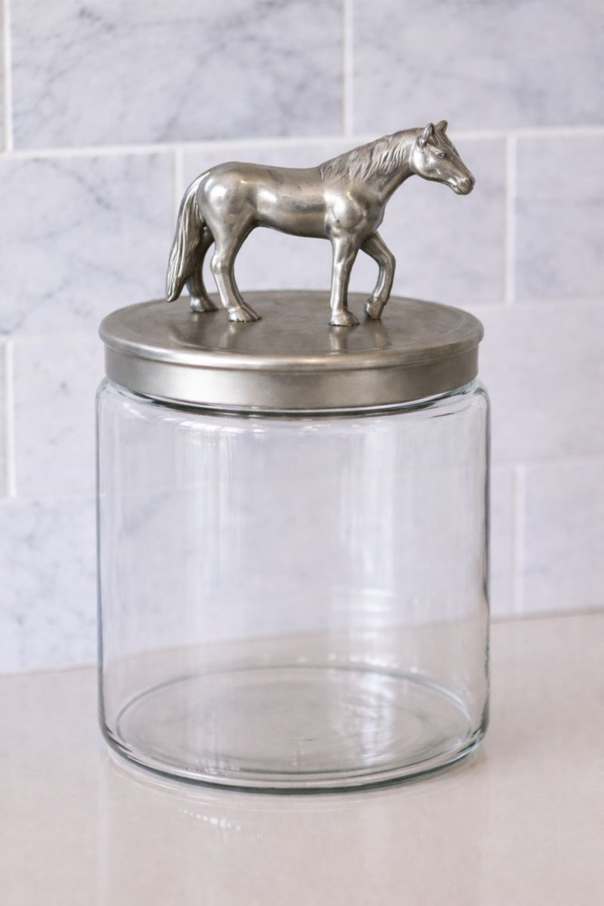 Clear glass storage jar with a brushed silver aluminum lid featuring a sculpted horse accent.