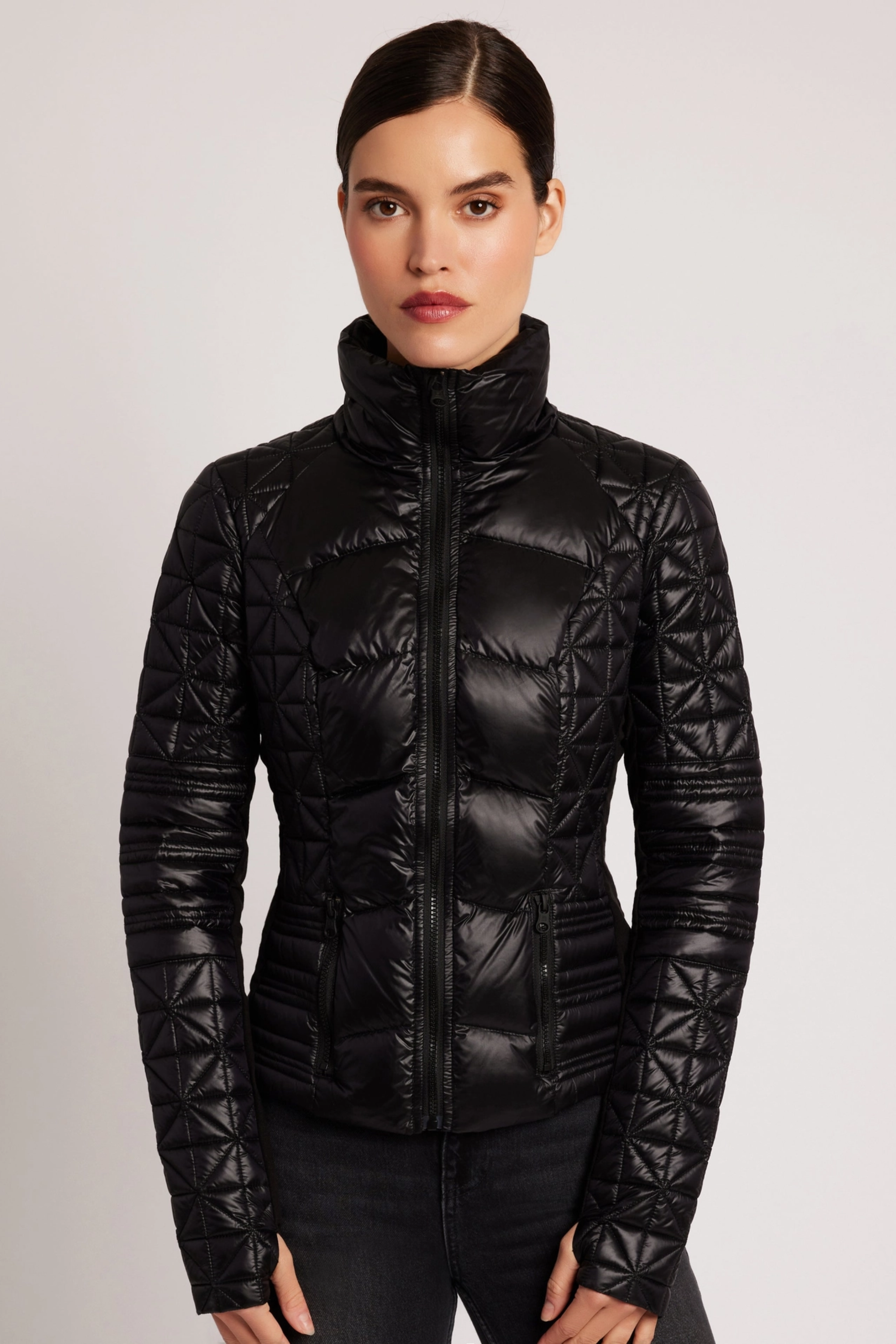 Woman wearing a black quilted jacket against a plain background - Packable puffer jacket, Lightweight down jacket, Black athletic outerwear, Travel-friendly puffer coat, Stylish winter layering