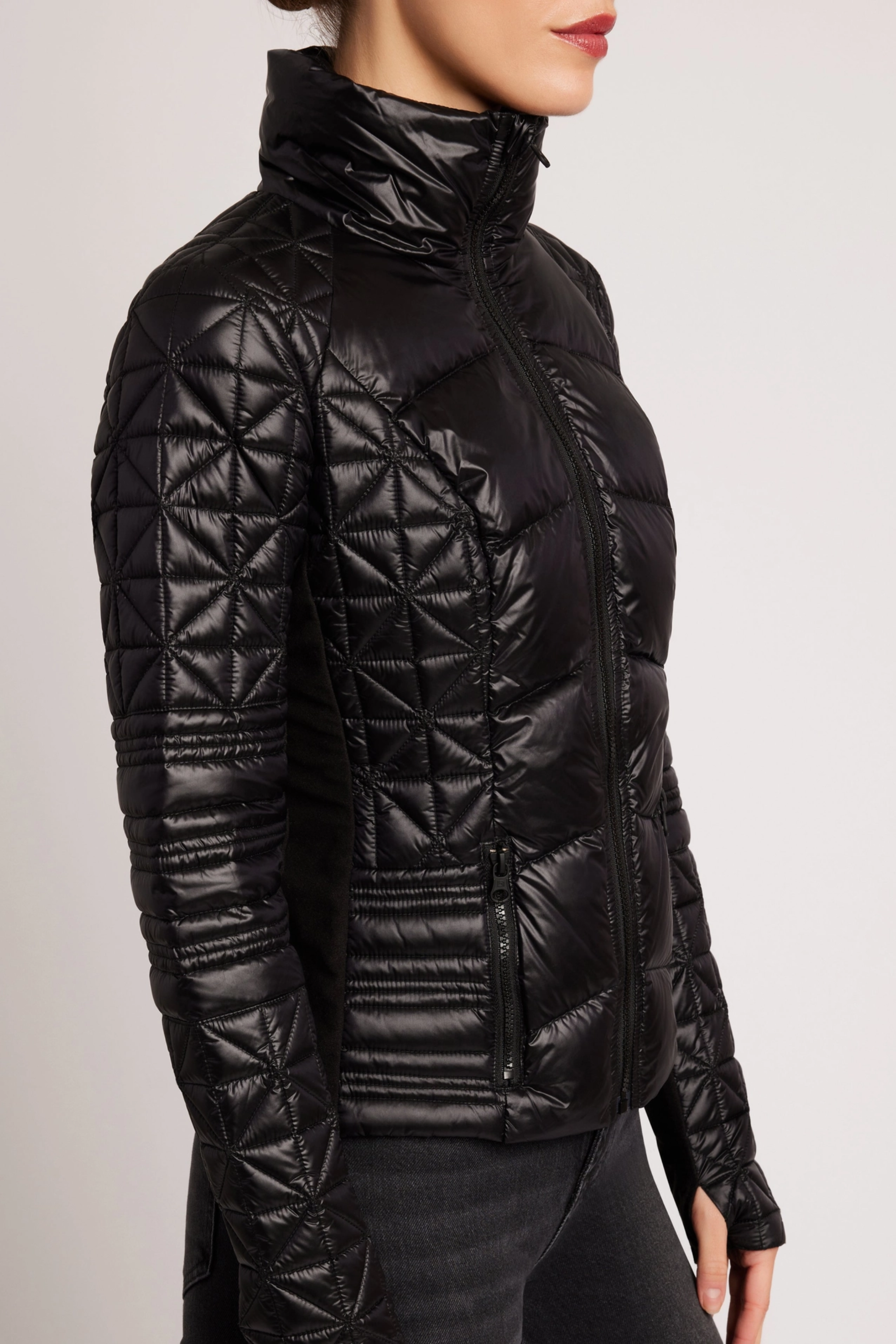Woman wearing a black quilted jacket against a plain background - Packable puffer jacket, Lightweight down jacket, Black athletic outerwear, Travel-friendly puffer coat, Stylish winter layering
