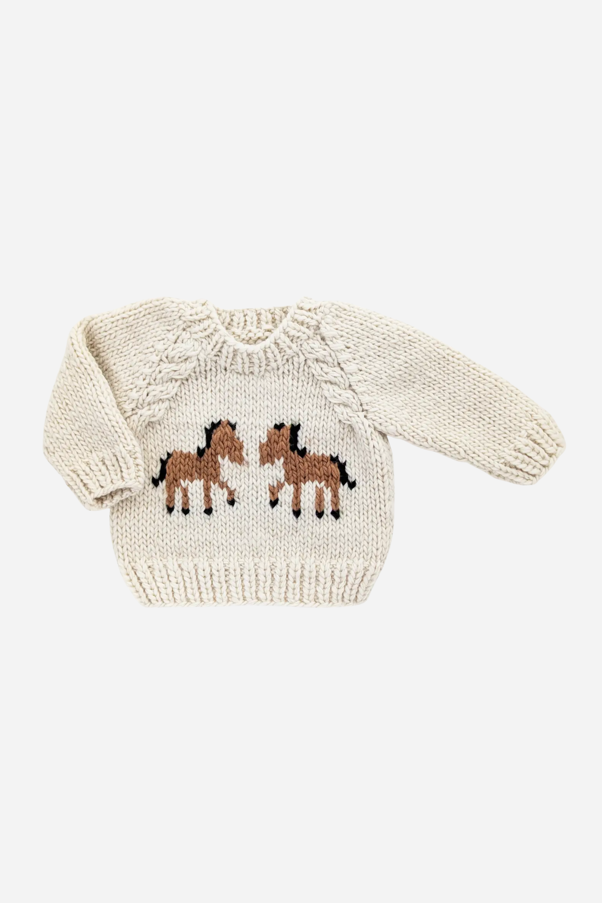 Cream, hand-knit pony sweater made of soft, sustainable yarn with two brown horses facing each other on the front, raglan sleeves, and cable accents. Cozy, playful design conveys warmth and charm, photographed against a plain background.