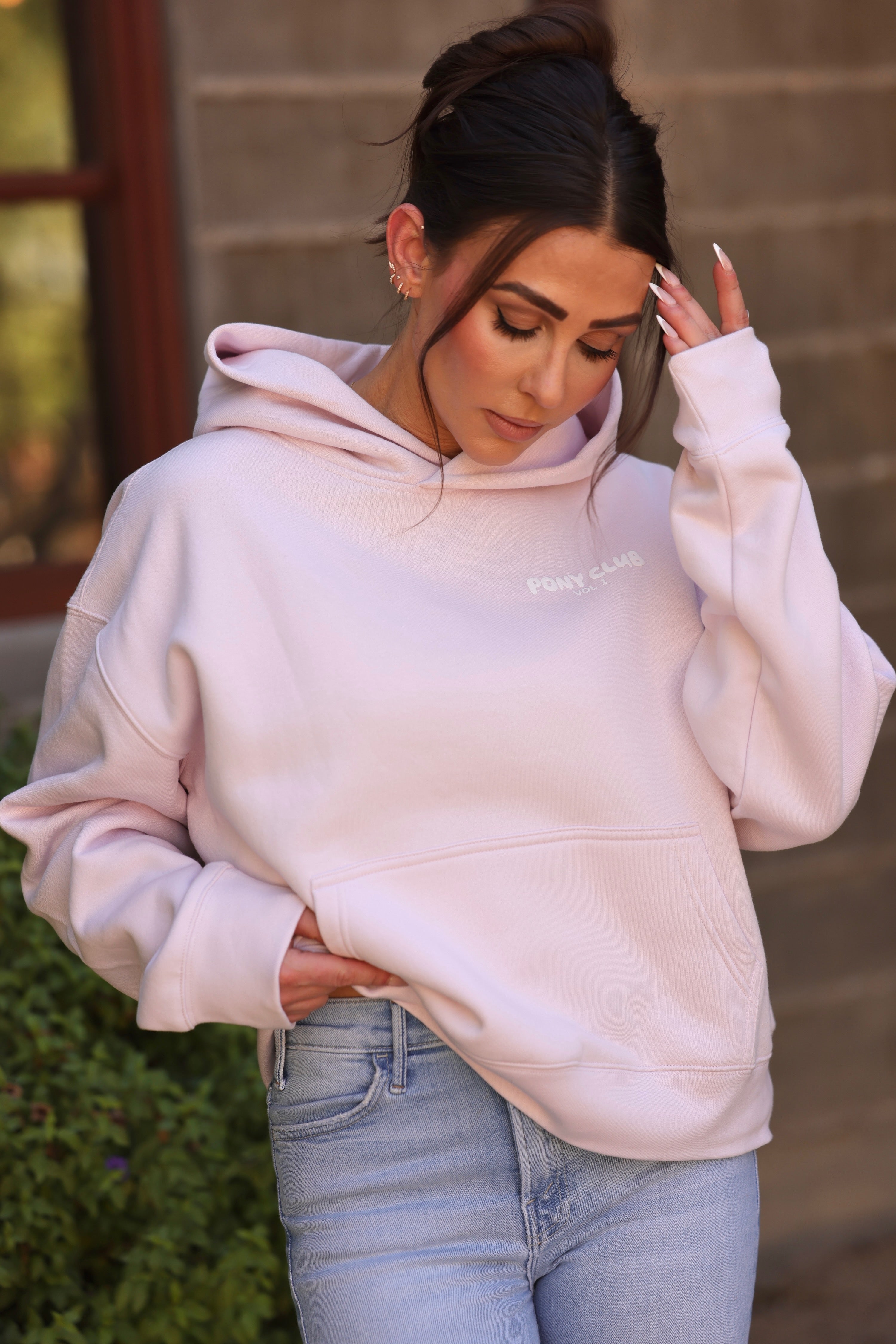 Close-up of a person wearing a light petal pink hoodie with "PONY CLUB VOL. 1" in white text. The fabric appears soft, conveying a cozy feel.