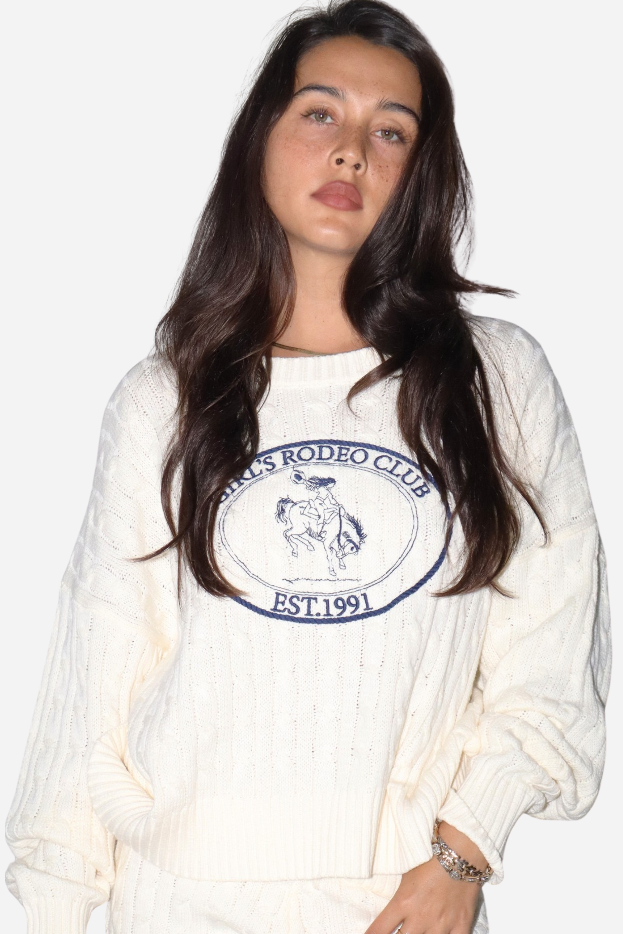 The Girls Rodeo Club Sweater blends classic varsity style with timeless equestrian charm. Designed with a relaxed dropped-shoulder silhouette and finished with textured cable-knit detailing, this cozy knit delivers effortless western sophistication, whether you're at the barn, in town, or layered for cool spring rides. Featuring navy embroidered varsity lettering across a soft cream knit, this sweater captures the spirit of rodeo heritage with a modern cowgirl feel.