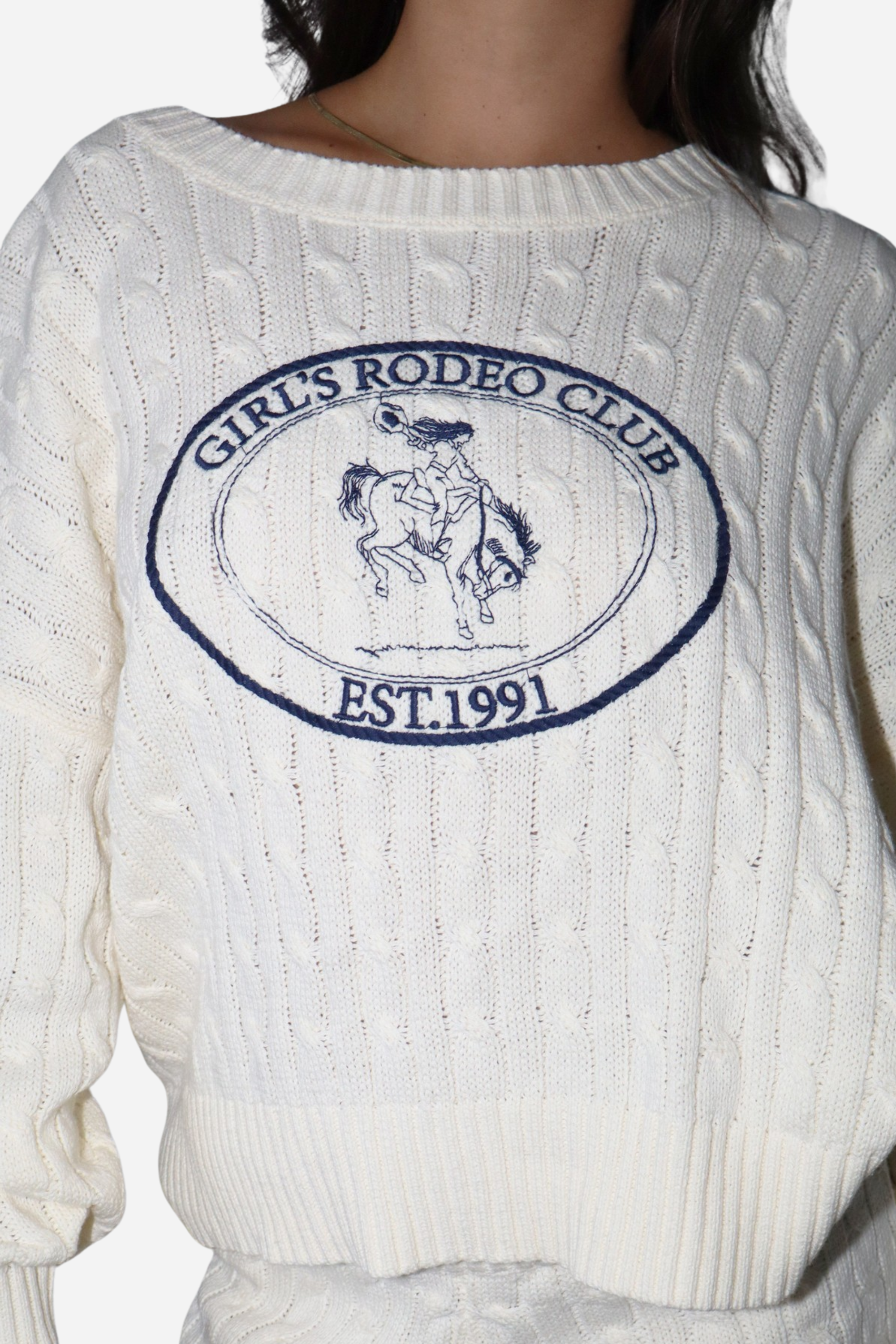 The Girls Rodeo Club Sweater blends classic varsity style with timeless equestrian charm. Designed with a relaxed dropped-shoulder silhouette and finished with textured cable-knit detailing, this cozy knit delivers effortless western sophistication, whether you're at the barn, in town, or layered for cool spring rides. Featuring navy embroidered varsity lettering across a soft cream knit, this sweater captures the spirit of rodeo heritage with a modern cowgirl feel.