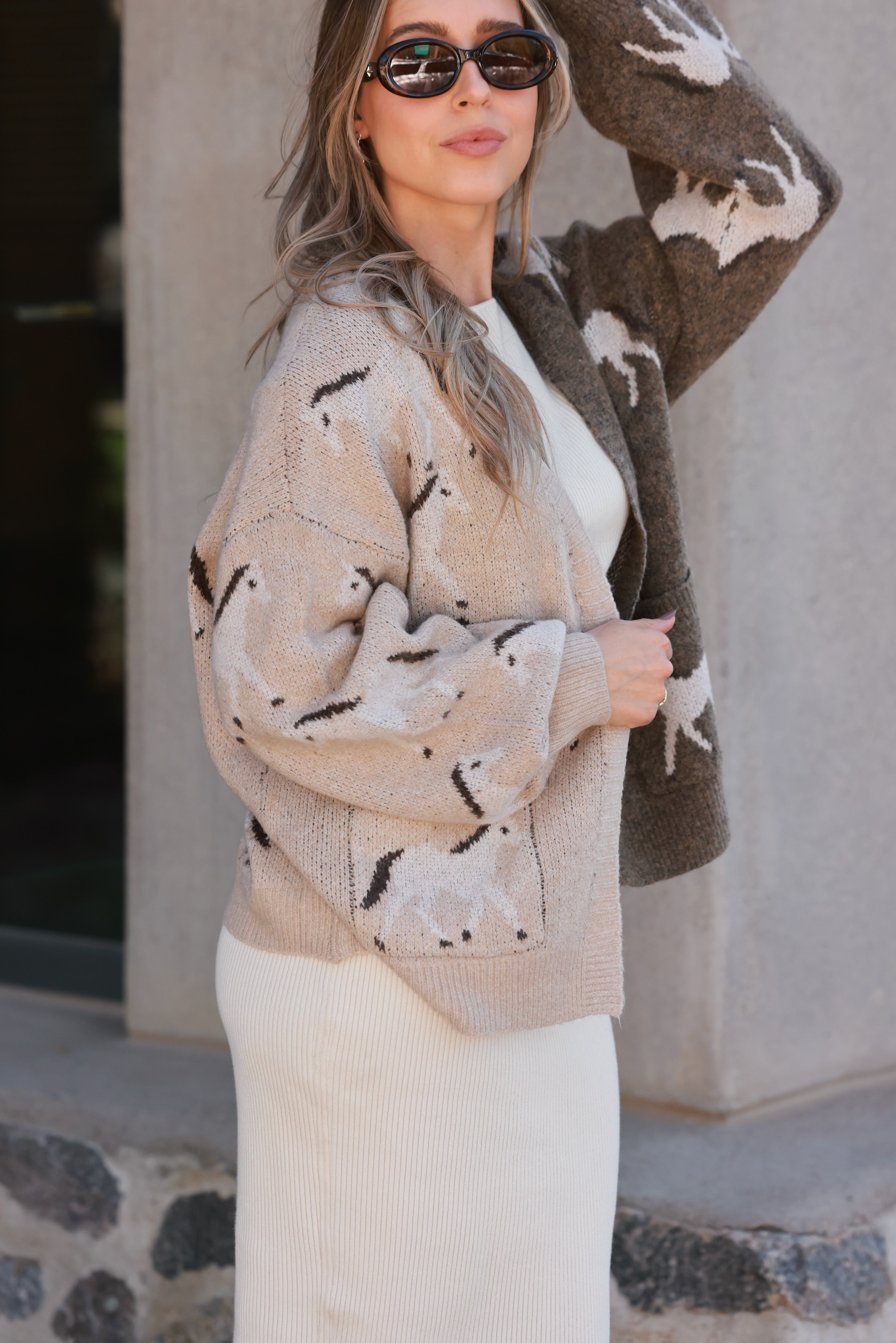 Woman wearing an asymmetric open-front cardigan in brown and beige with white horse patterns. This cozy equestrian cardigan blends rustic western style with casual horse girl apparel, soft, stretchy knit perfect for everyday wear.