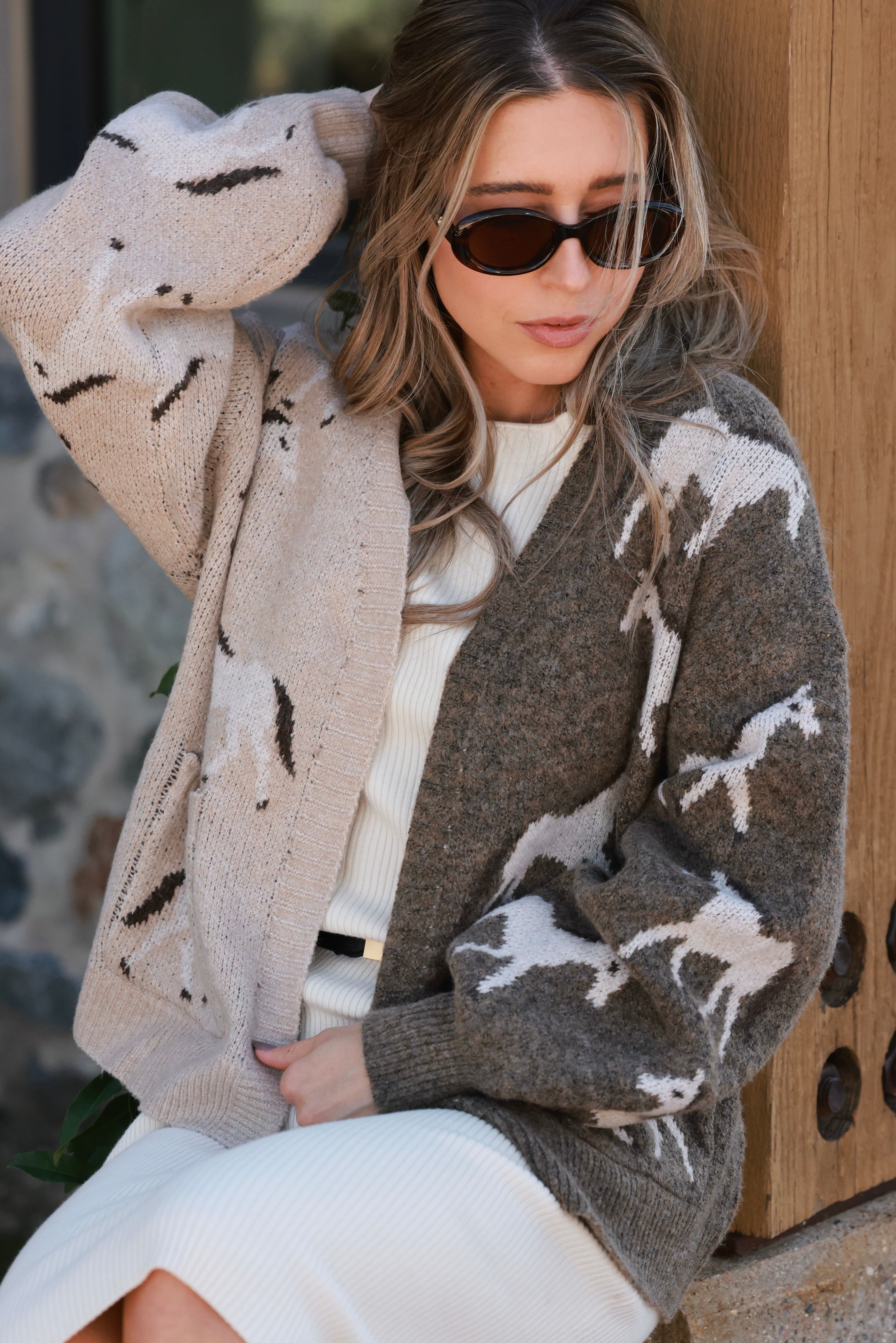 Woman wearing an asymmetric open-front cardigan in brown and beige with white horse patterns. This cozy equestrian cardigan blends rustic western style with casual horse girl apparel, soft, stretchy knit perfect for everyday wear.
