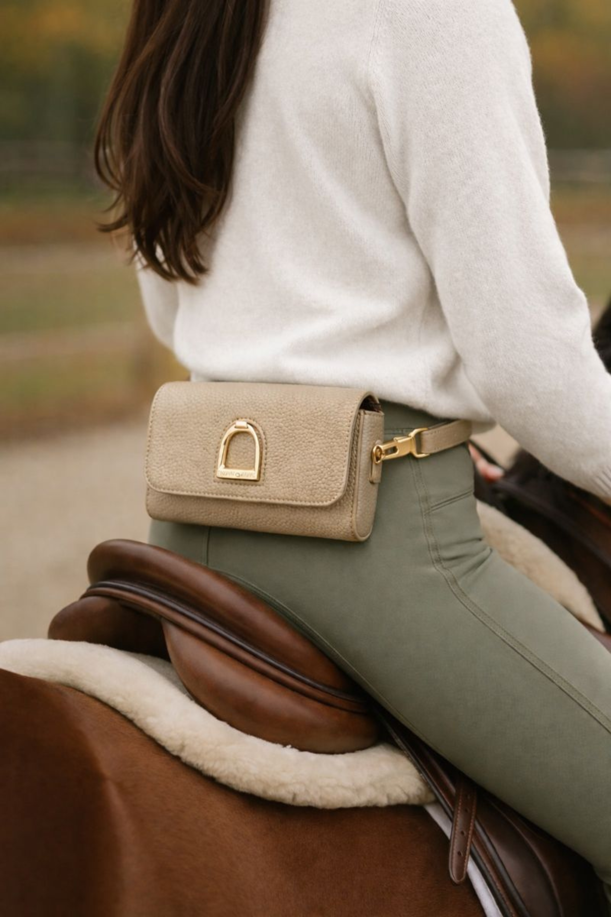 Equestrian leather belt bag made from pebbled leather with a gold stirrup emblem, interchangeable wristlet and adjustable straps, and lined interior.