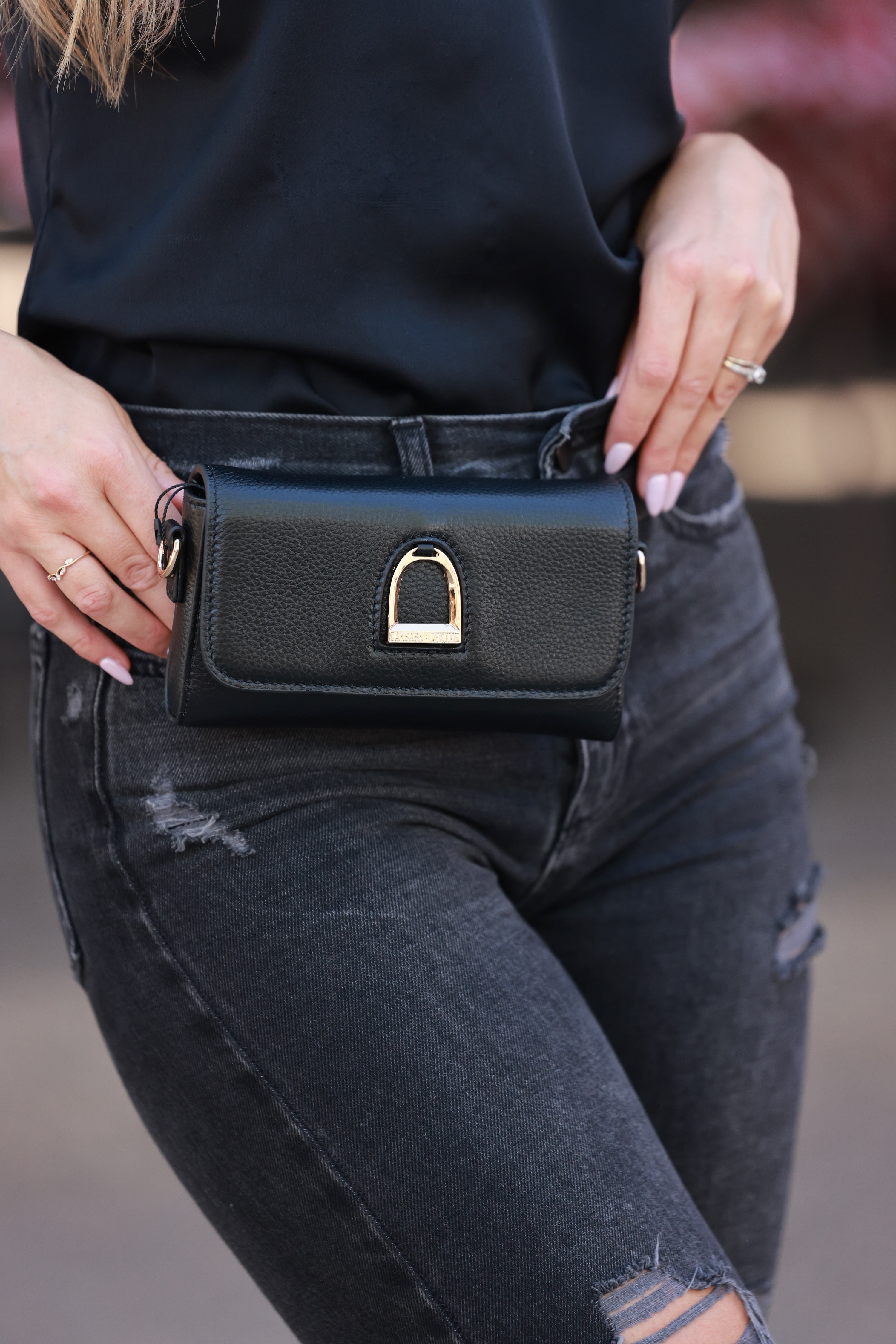 Person wearing a black leather waist bag with a gold clasp. - Horse stirrup belt bag, Equestrian-inspired belt bag,&stirrup detail belt bag