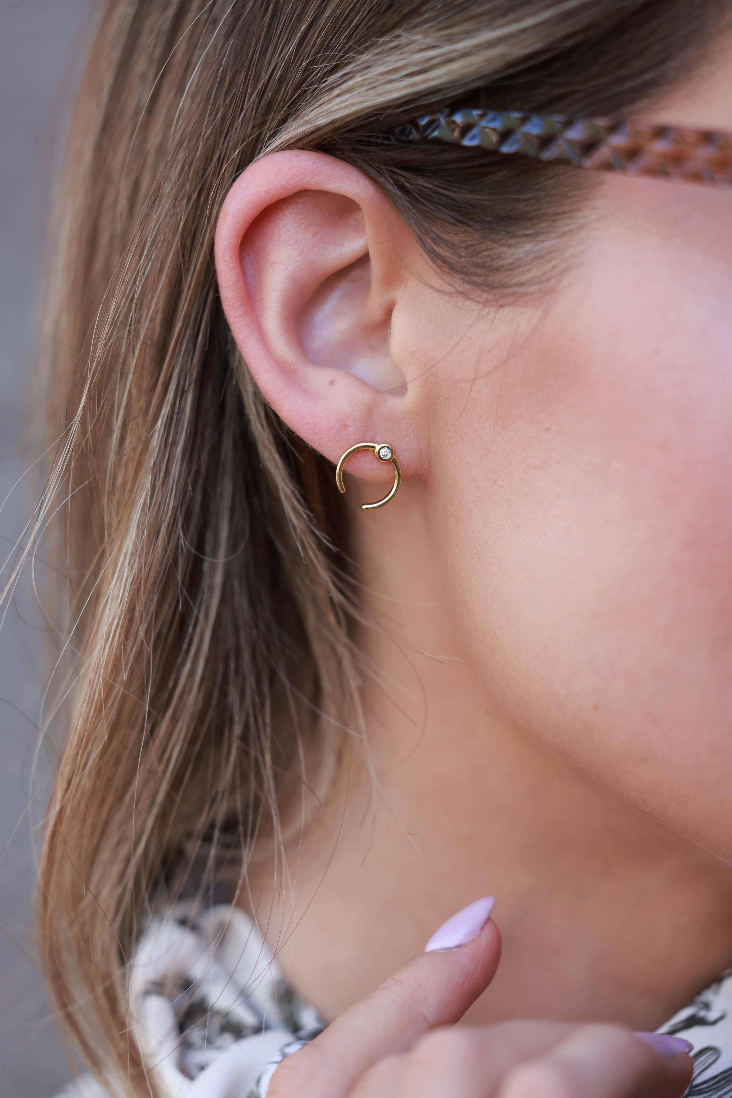 Close-up of a person wearing a gold hoop earring with a neutral background - equestrian inspired jewelry, horse girl accessories, dainty equestrian jewelry, horseshoe inspired design, small gifts for horse girls