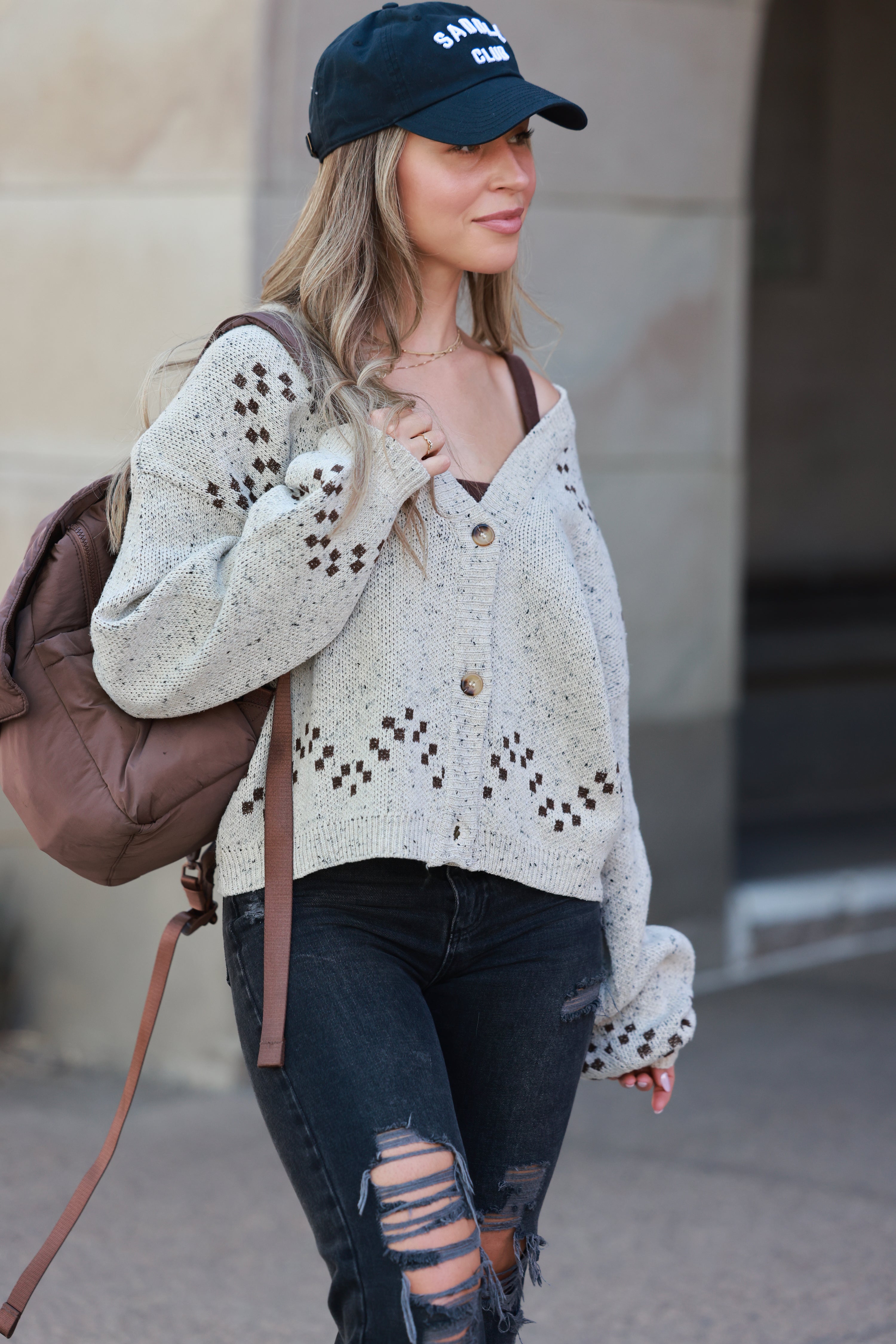 Woman wearing a patterned cardigan and ripped jeans with a backpack, standing against a neutral background. - Horse graphic cardigan, Western button down sweater, Equestrian fall knit, Oatmeal horse print cardigan, Cowgirl boutique sweater