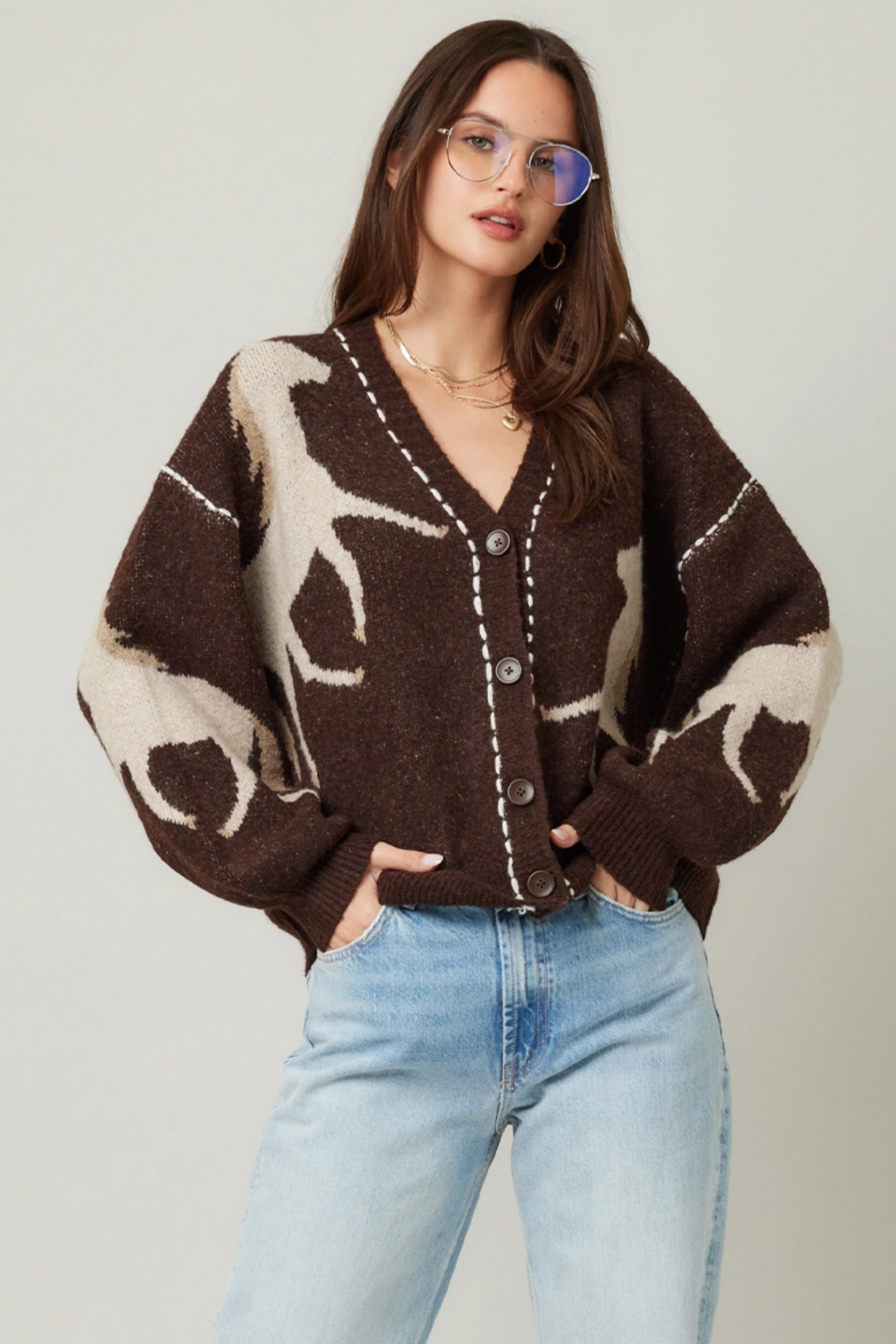 Woman wearing a brown cardigan with deer pattern and light blue jeans on a plain background - Horse knit cardigan, Brown western cardigan, Cowgirl graphic sweater, Oversized horse print cardigan, Equestrian boutique knitwear