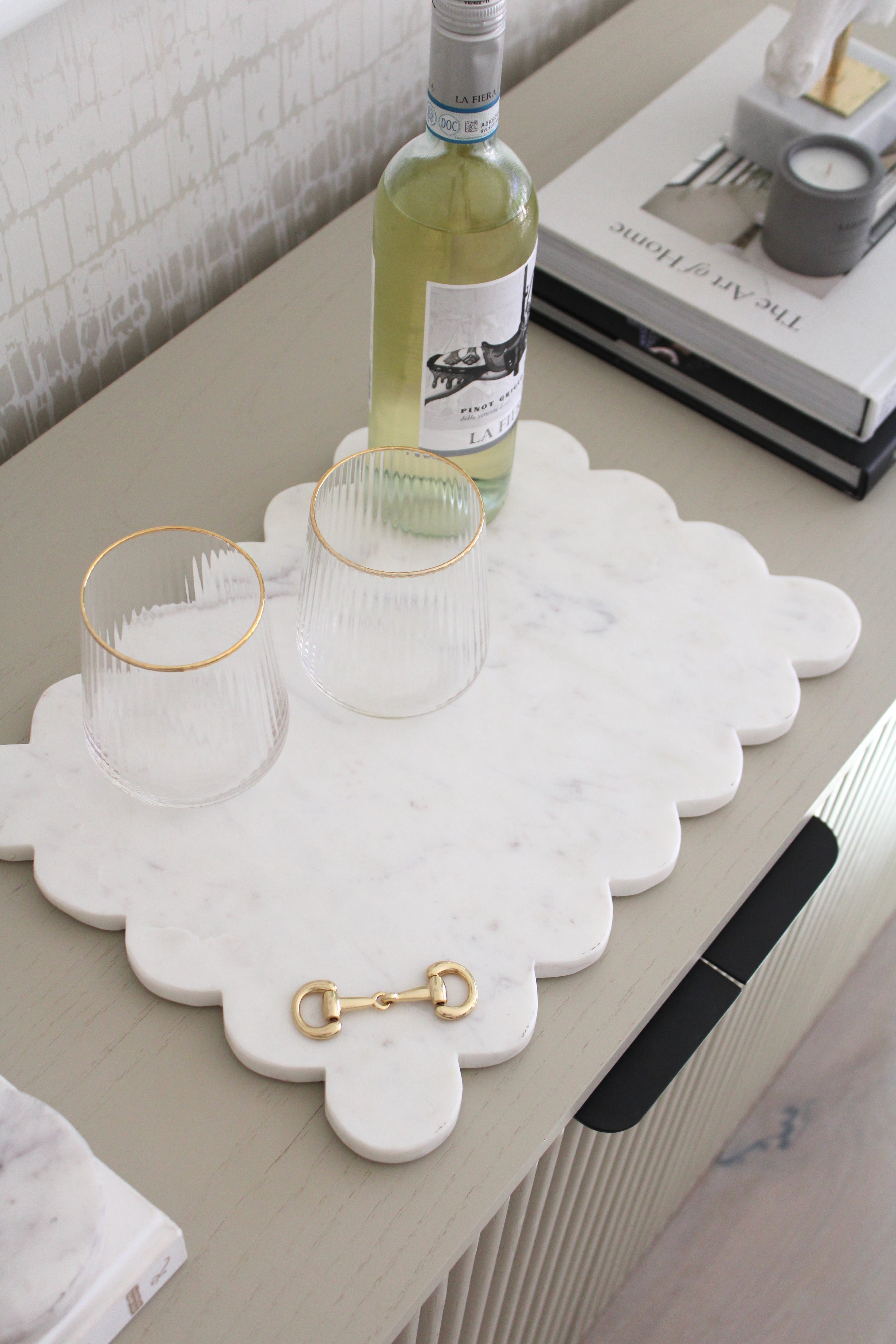 Elegant white marble scalloped serving board with gold D-ring bit, styled in an equestrian-themed kitchen. The handcrafted marble board features subtle natural veining and polished gold hardware, displayed with cheese, fruits, and wine accents. Perfect as a horse-inspired charcuterie tray or decorative equestrian home accent.