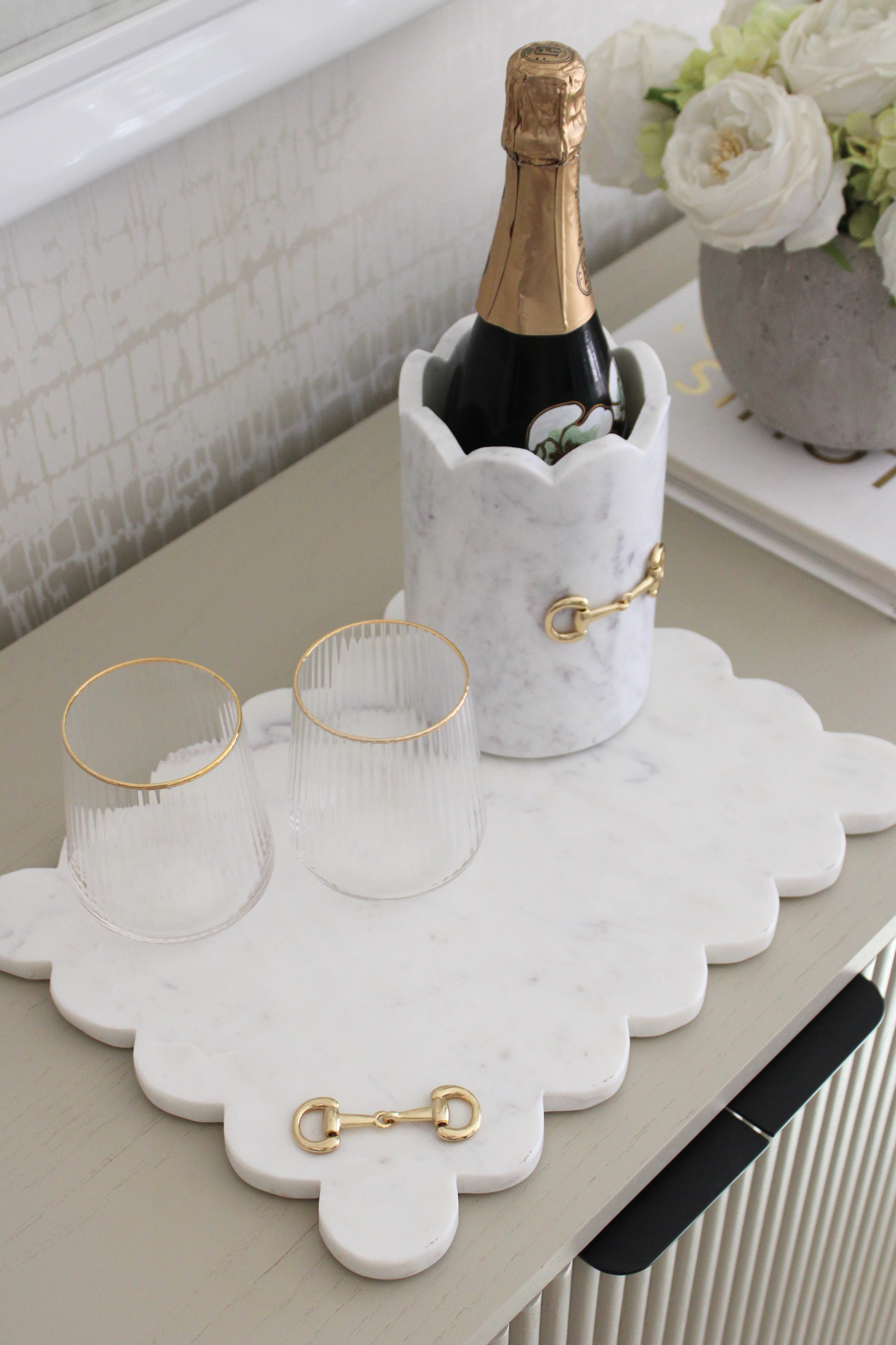 Elegant white marble scalloped serving board with gold D-ring bit, styled in an equestrian-themed kitchen. The handcrafted marble board features subtle natural veining and polished gold hardware, displayed with cheese, fruits, and wine accents. Perfect as a horse-inspired charcuterie tray or decorative equestrian home accent.