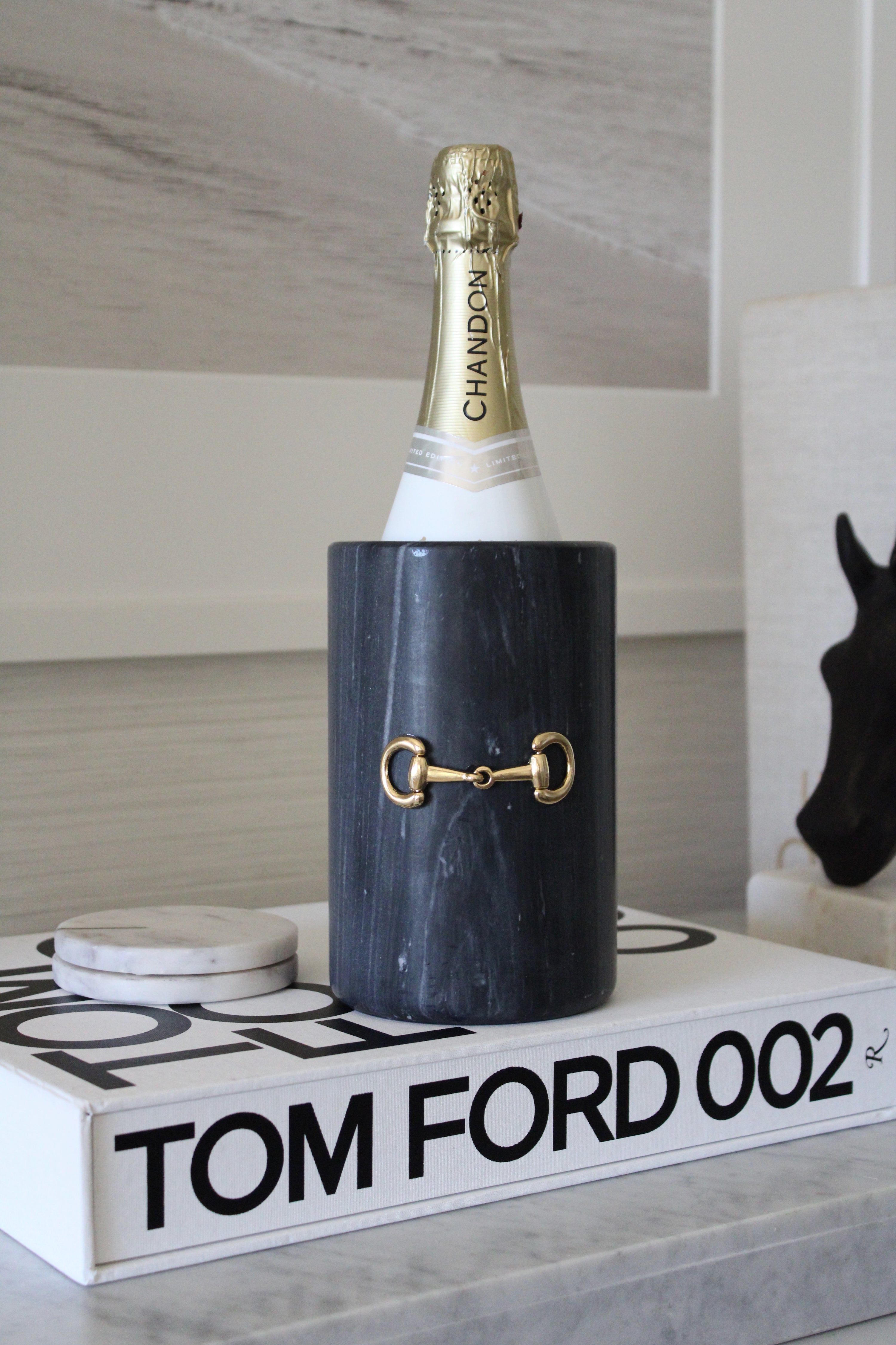 Handcrafted black marble D-ring cylinder with polished gold horse bit hardware, styled in an elegant equestrian kitchen. The sleek matte marble vessel doubles as a wine chiller, utensil holder, or flower vase, featuring natural veining and timeless horse-inspired detailing for a sophisticated home accent.