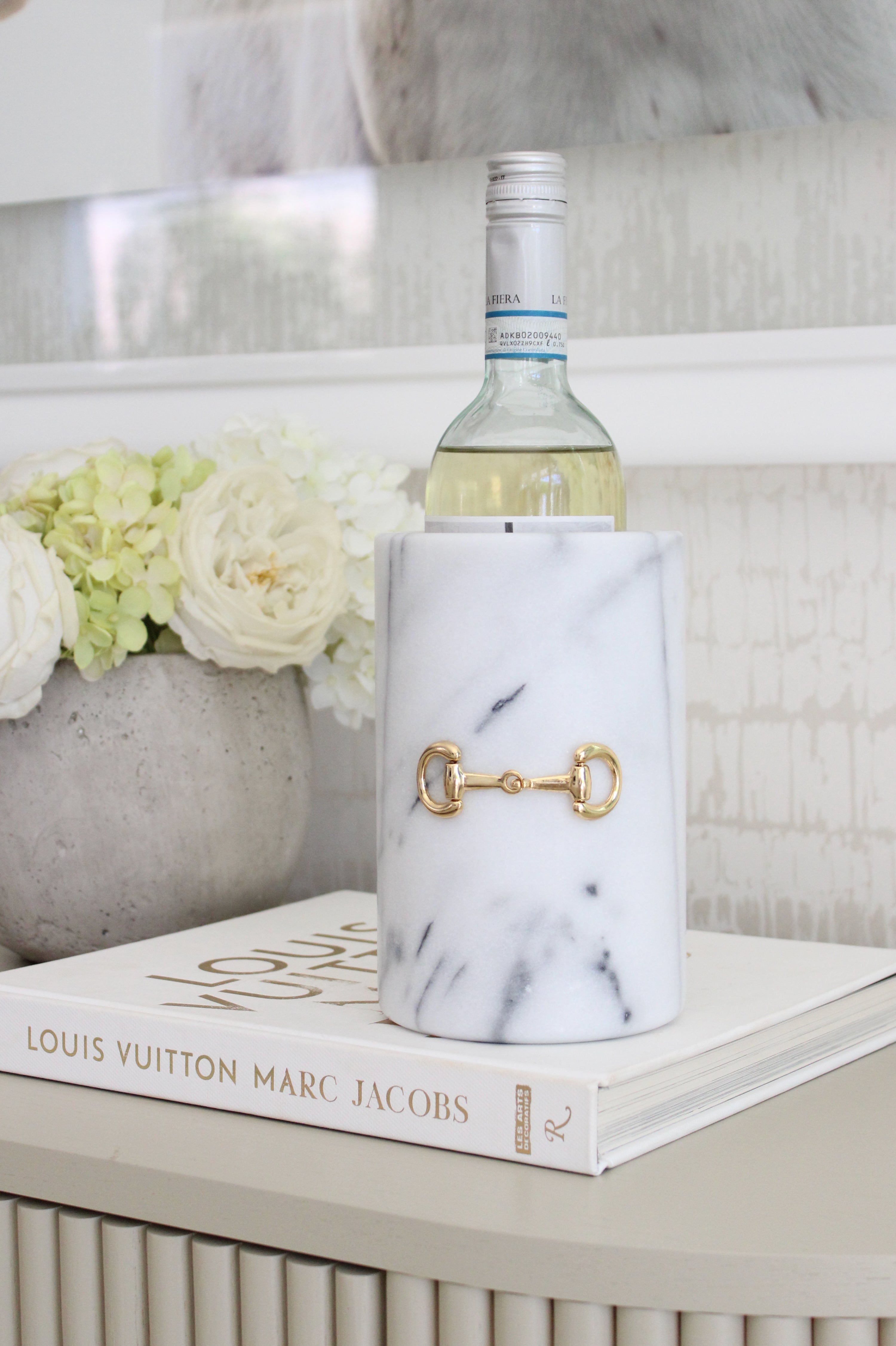 Handcrafted white marble D-ring cylinder with polished gold horse bit hardware, styled in an elegant equestrian kitchen. The sleek matte marble vessel doubles as a wine chiller, utensil holder, or flower vase, featuring natural veining and timeless horse-inspired detailing for a sophisticated home accent.