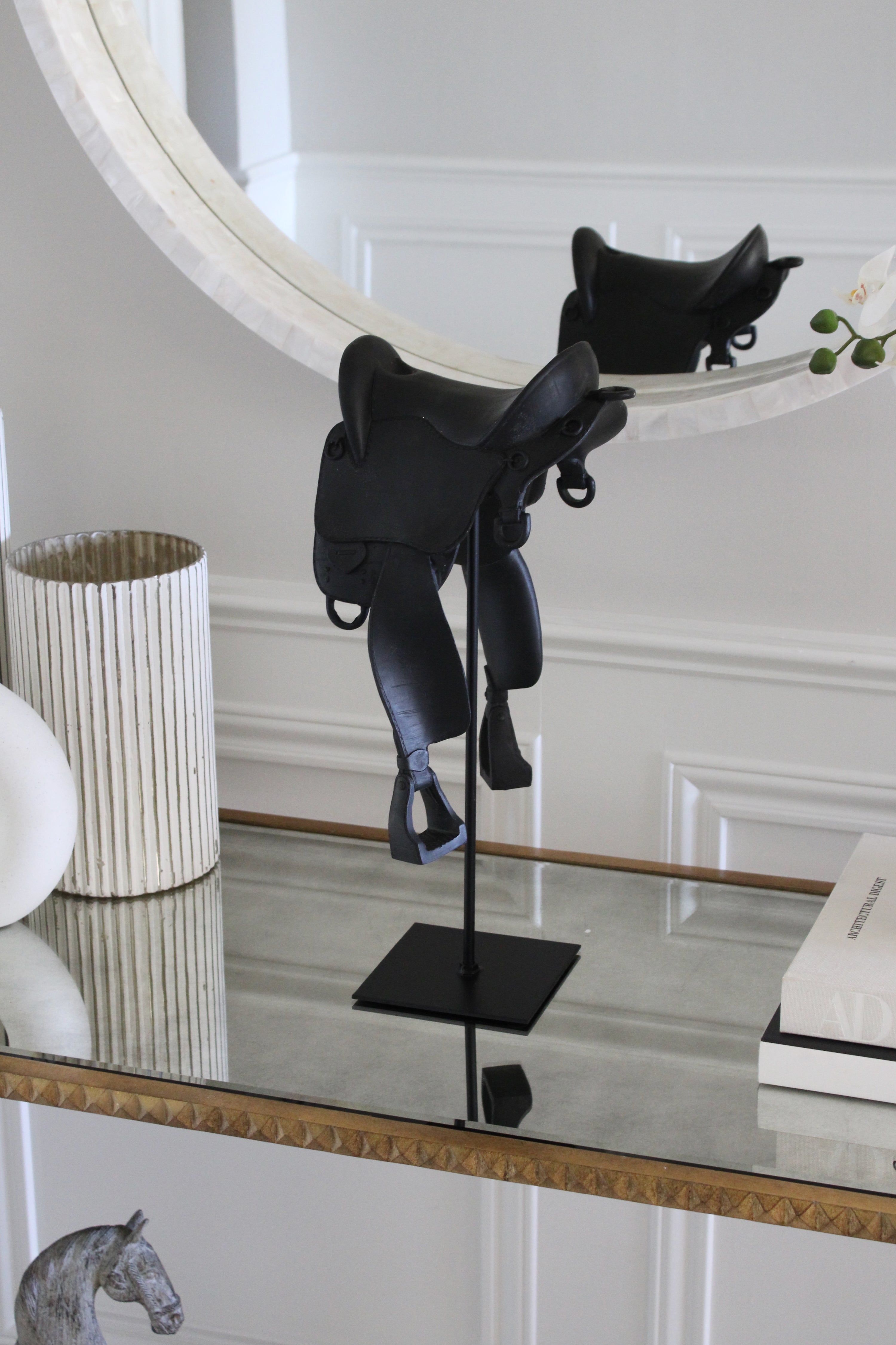 Black English-style horse saddle decor piece crafted from matte-finish resin and metal detailing. Mounted on a black metal stand with a square base, this modern equestrian sculpture captures the elegance of traditional riding saddles and adds a bold statement to home or office décor.